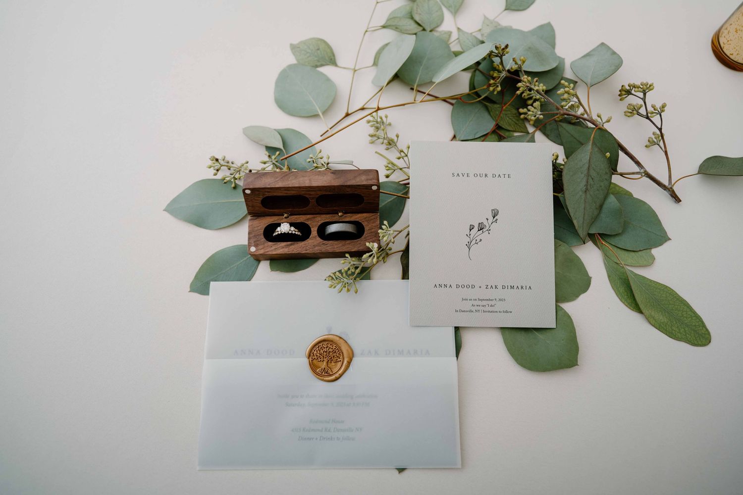 Wedding stationery with wax seal envelope, ring box, and eucalyptus greenery flat lay.