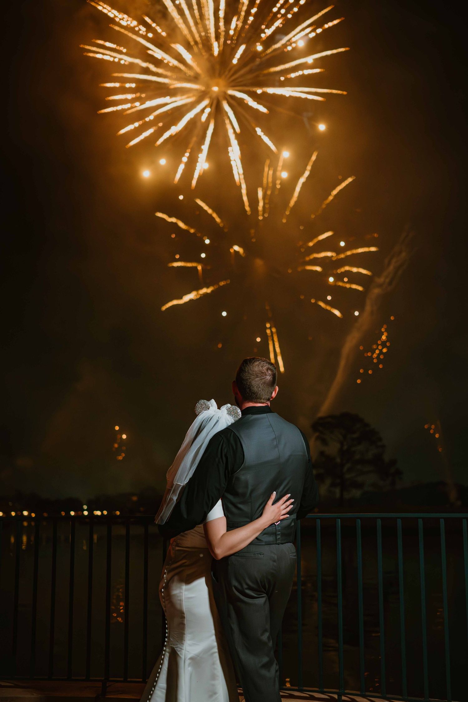 Bride and groom embrace while watching stunning golden fireworks display light up the night sky.