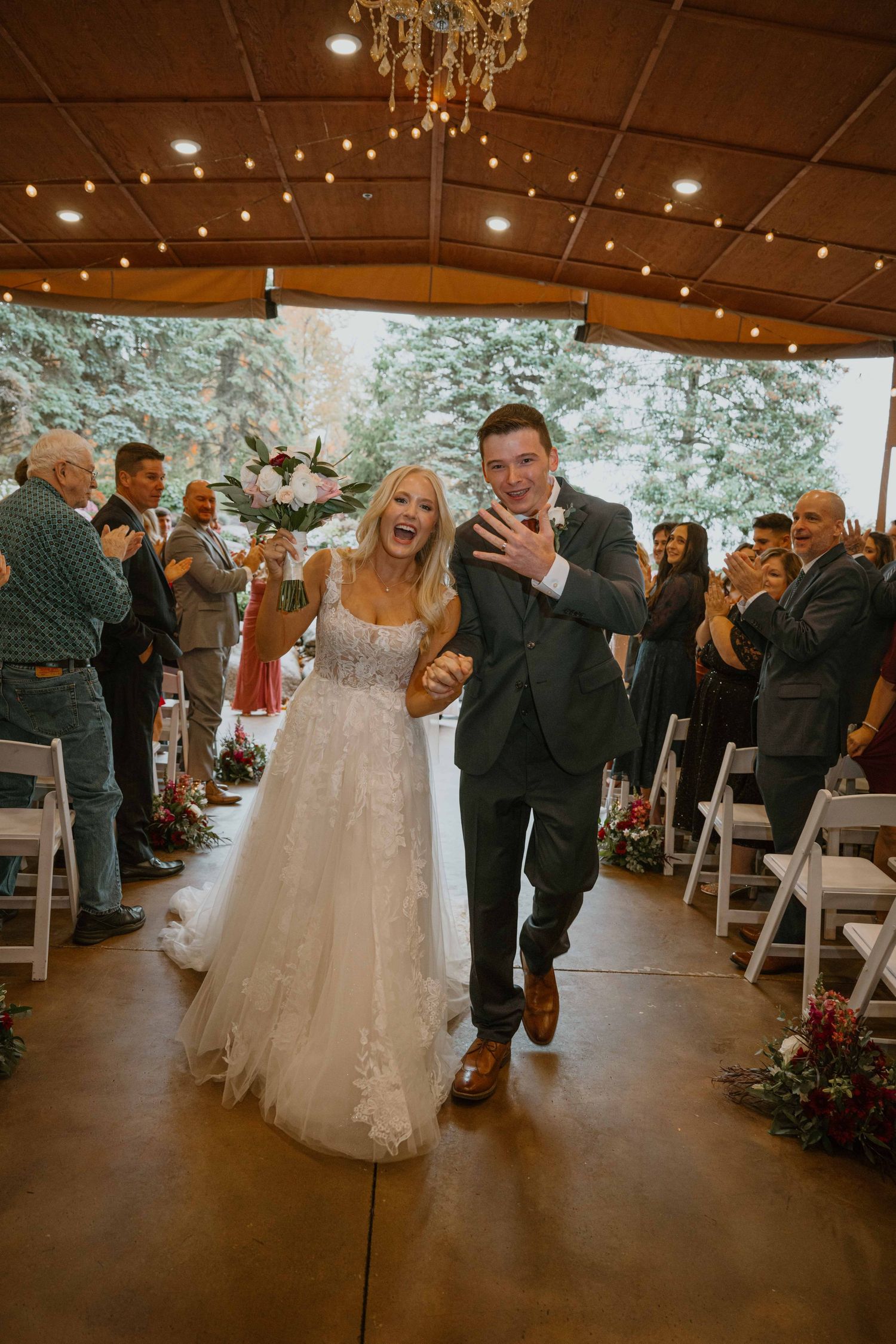 Joyful bride and groom walking back down the aisle after their wedding ceremony in a rustic venue.