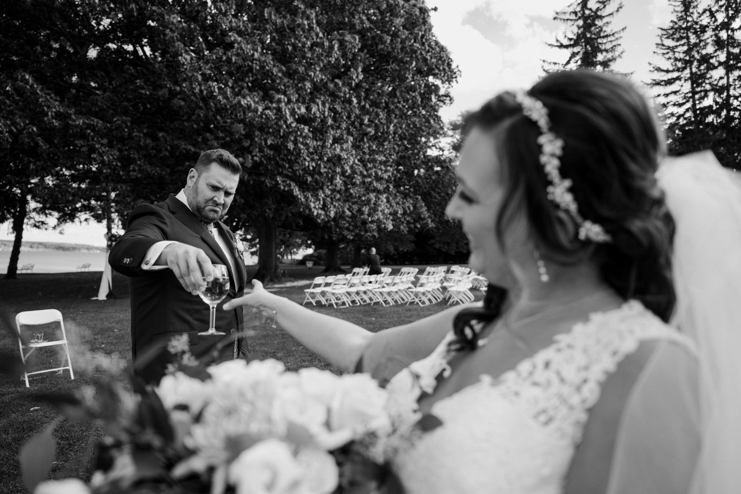 Black and white photo of groom pouring champagne for the bride during outdoor wedding portraits.