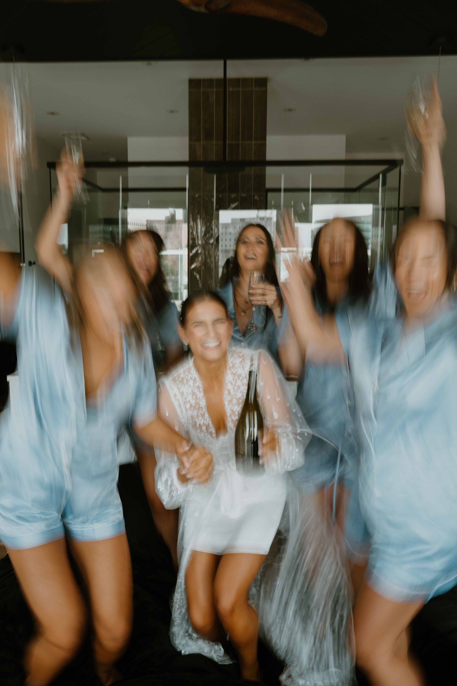 Motion-blur photo of bride in white robe celebrating with bridesmaids in blue pajamas.
