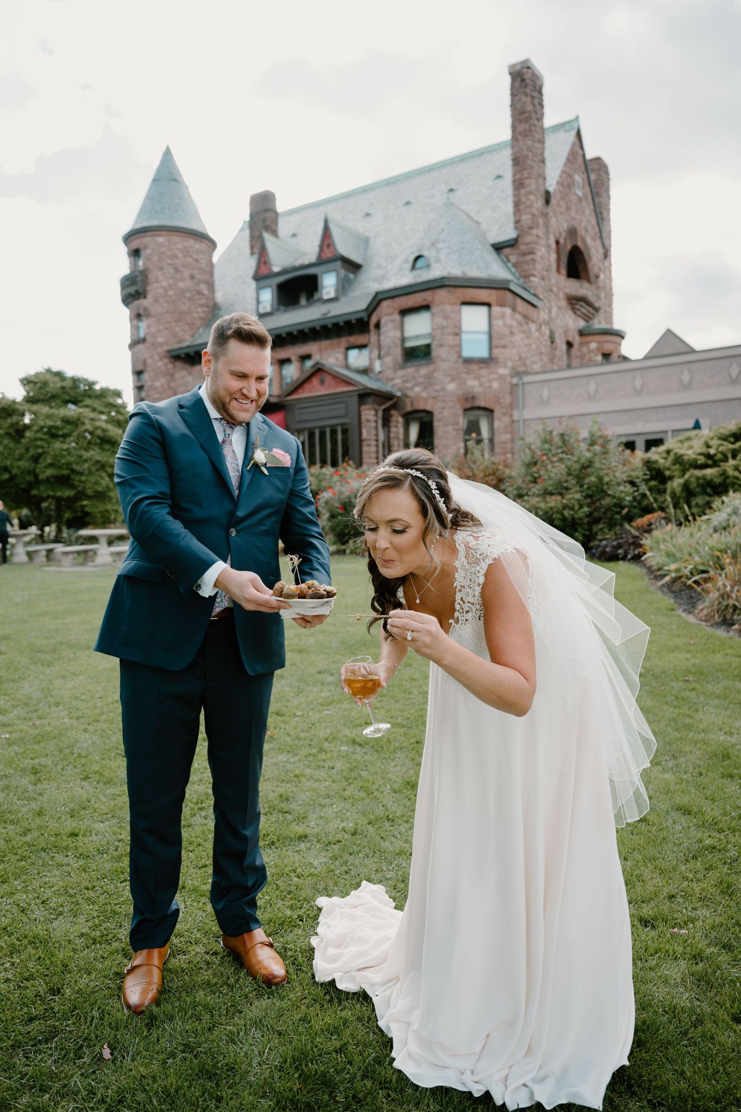 Bride and groom enjoying cocktail hour appetizers on the lawn of a stunning castle wedding venue.