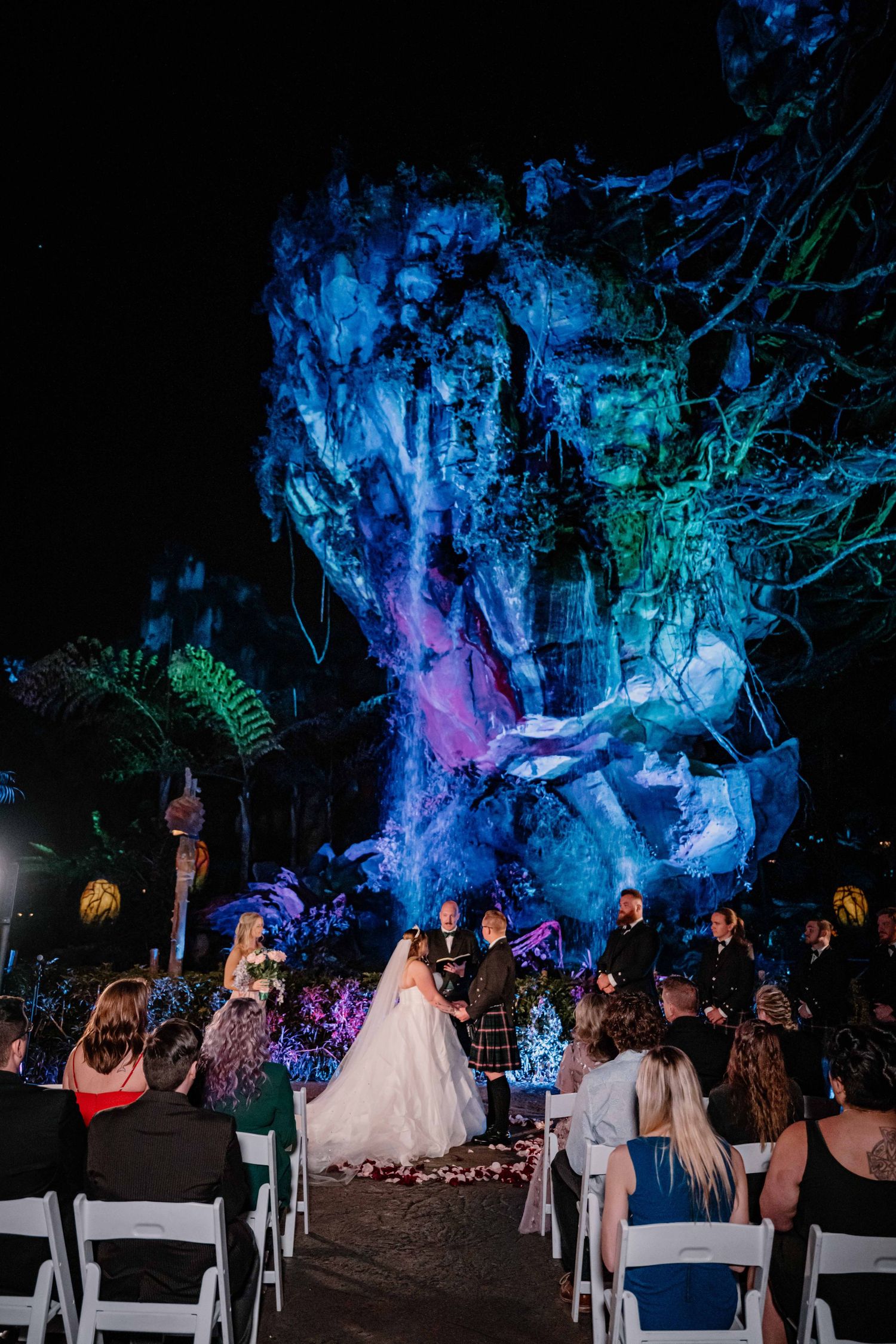 Outdoor wedding ceremony at night in Disney's Pandora - The World of Avatar with glowing blue rock formations.
