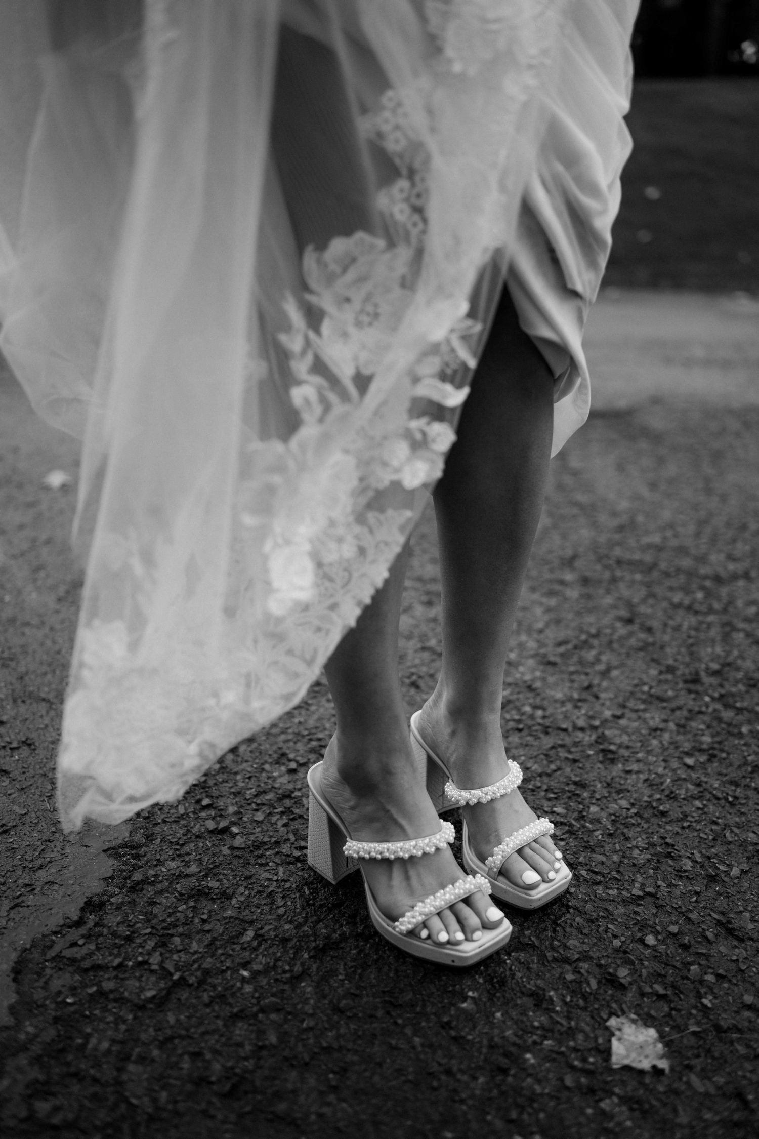 Black and white close-up of bride wearing pearl-strap block heel wedding sandals.
