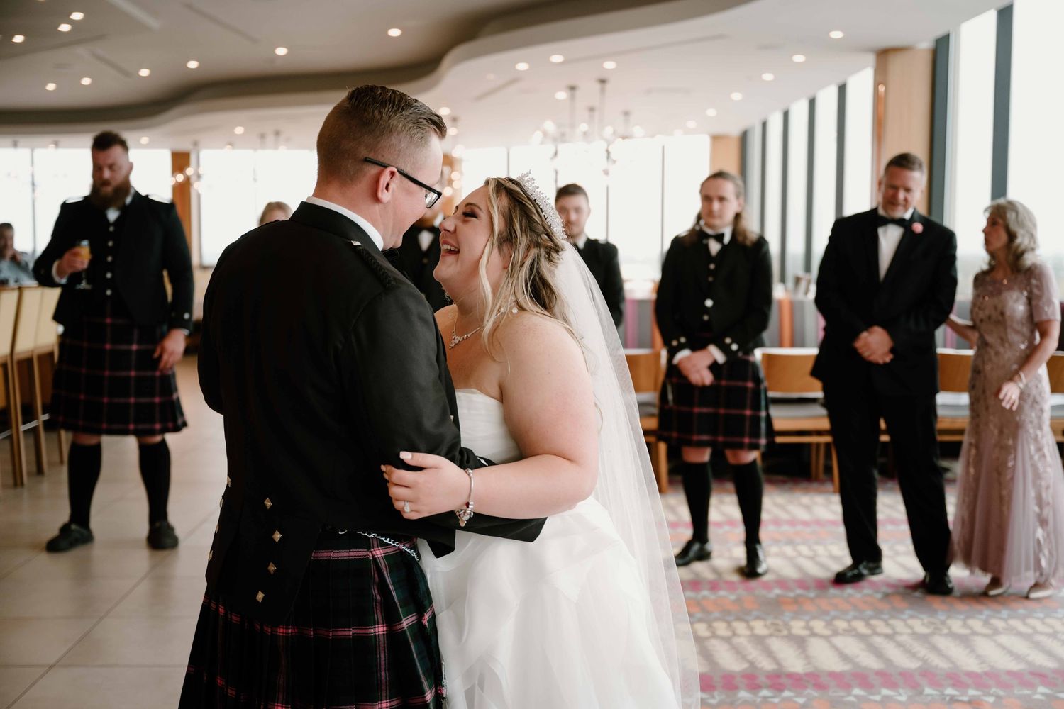 Groom in Scottish kilt shares first dance with bride at elegant wedding ceremony.
