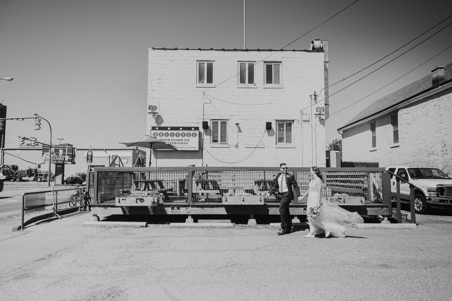 Black and white photo of bride and groom walking past construction equipment on a city street.