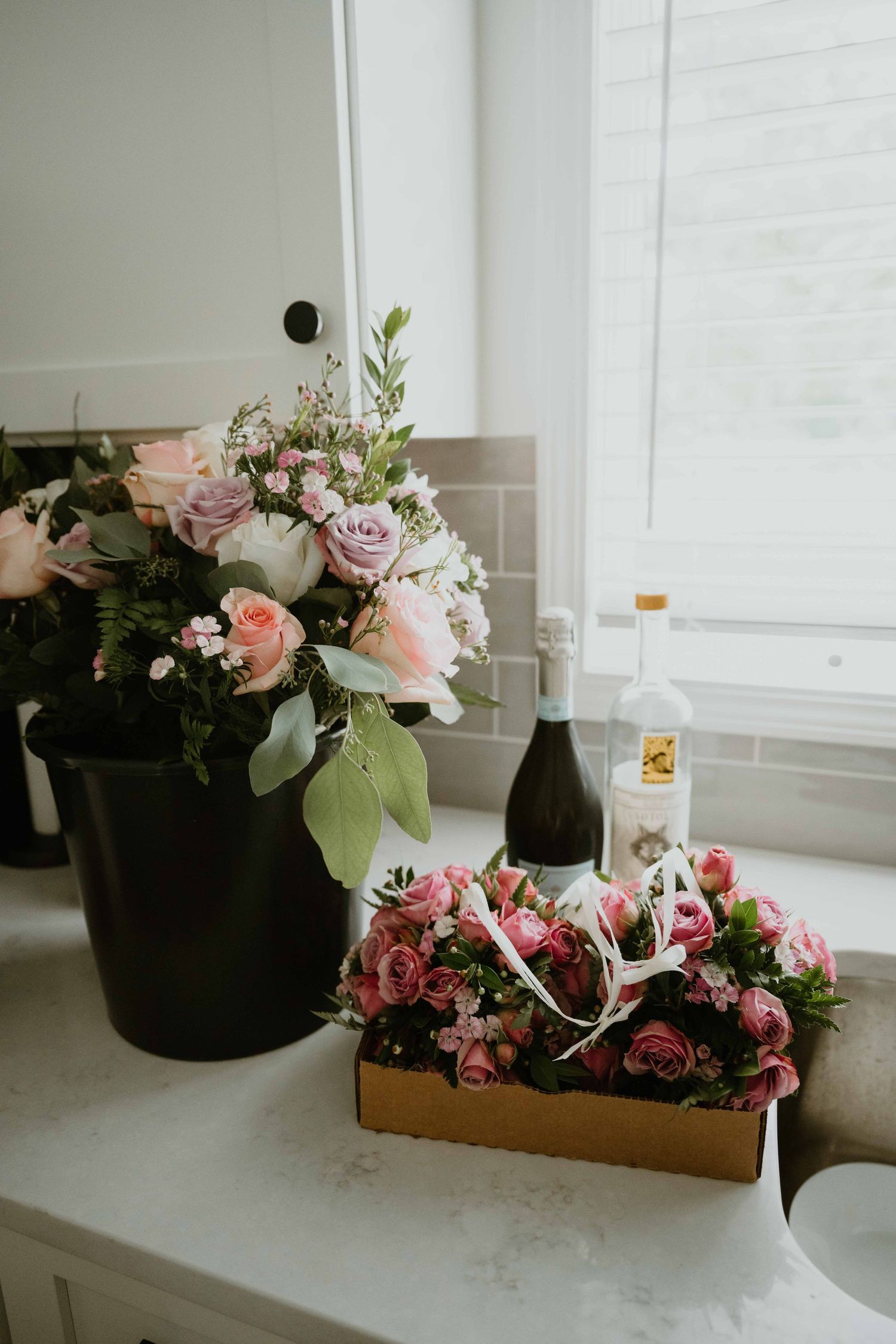Pink roses and wine bottle arranged on a marble countertop near a bright window.