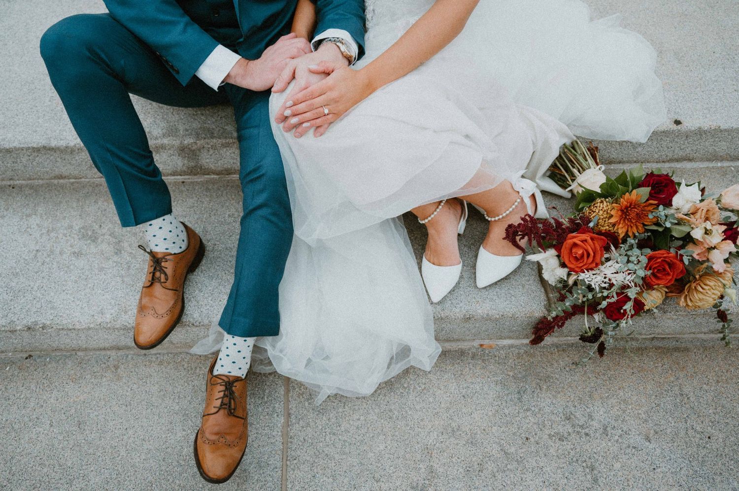 Close-up of bride and groom sitting on steps with colorful bouquet and grooms fun polka dot socks.