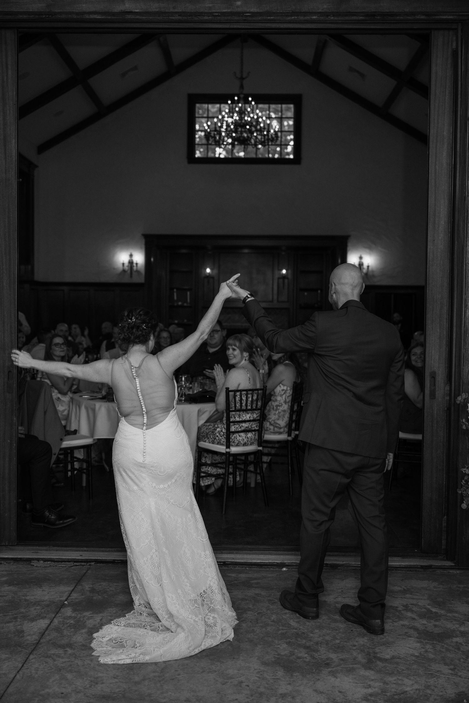 Black and white photo of bride and groom making grand entrance into rustic wedding reception hall.