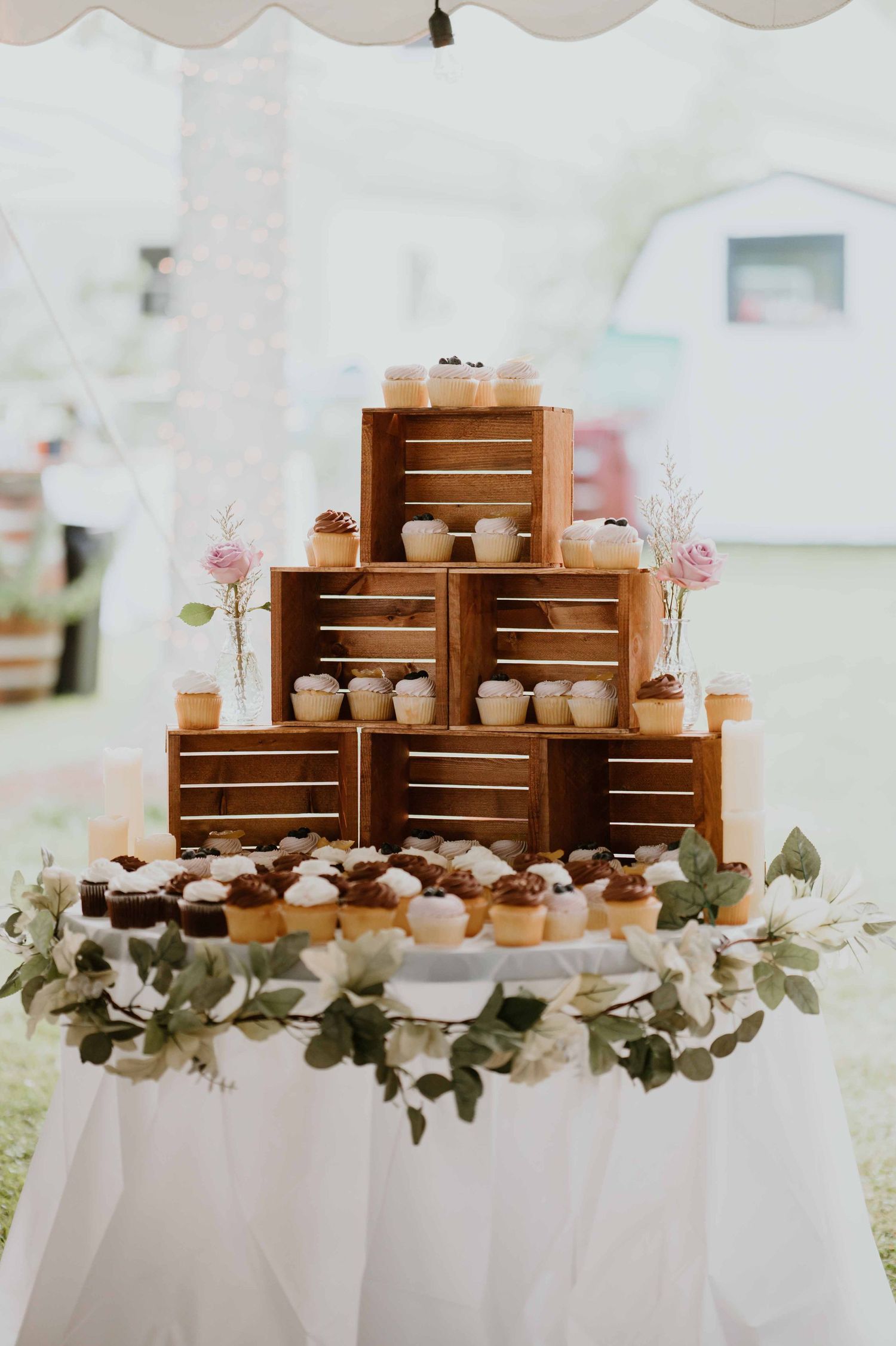 Rustic tiered cupcake display on wooden crates decorated with greenery at a wedding.