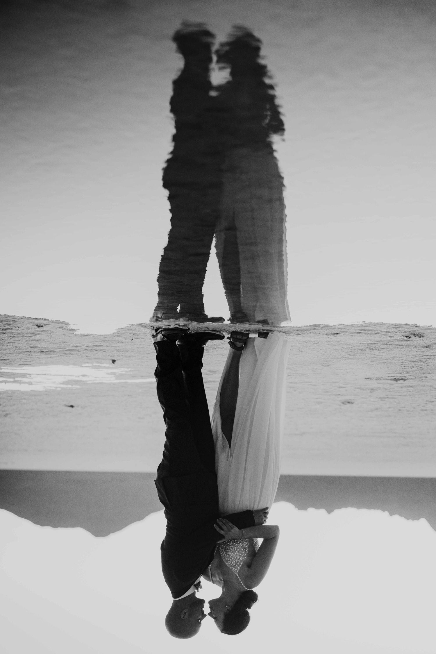 Black and white reflection of a kissing wedding couple mirrored in a thin pool on the salt flats.