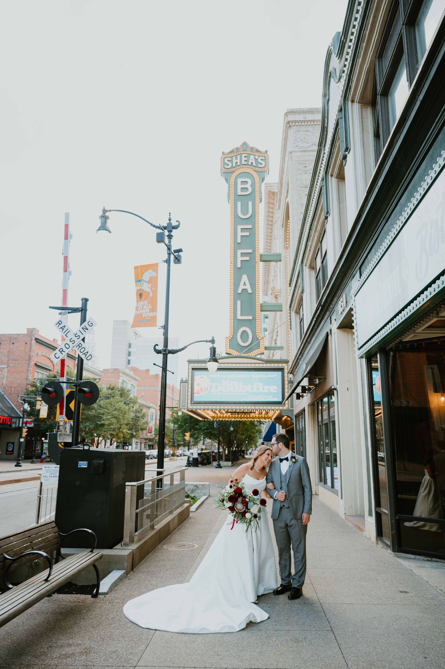 Bride and groom kissing on sidewalk beneath iconic Sheas Buffalo Theatre marquee sign.