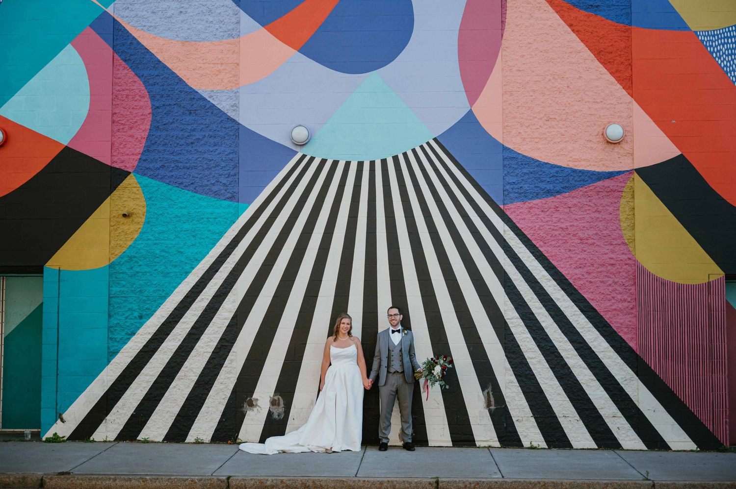 Bride and groom holding hands before bold black and white striped colorful street mural.