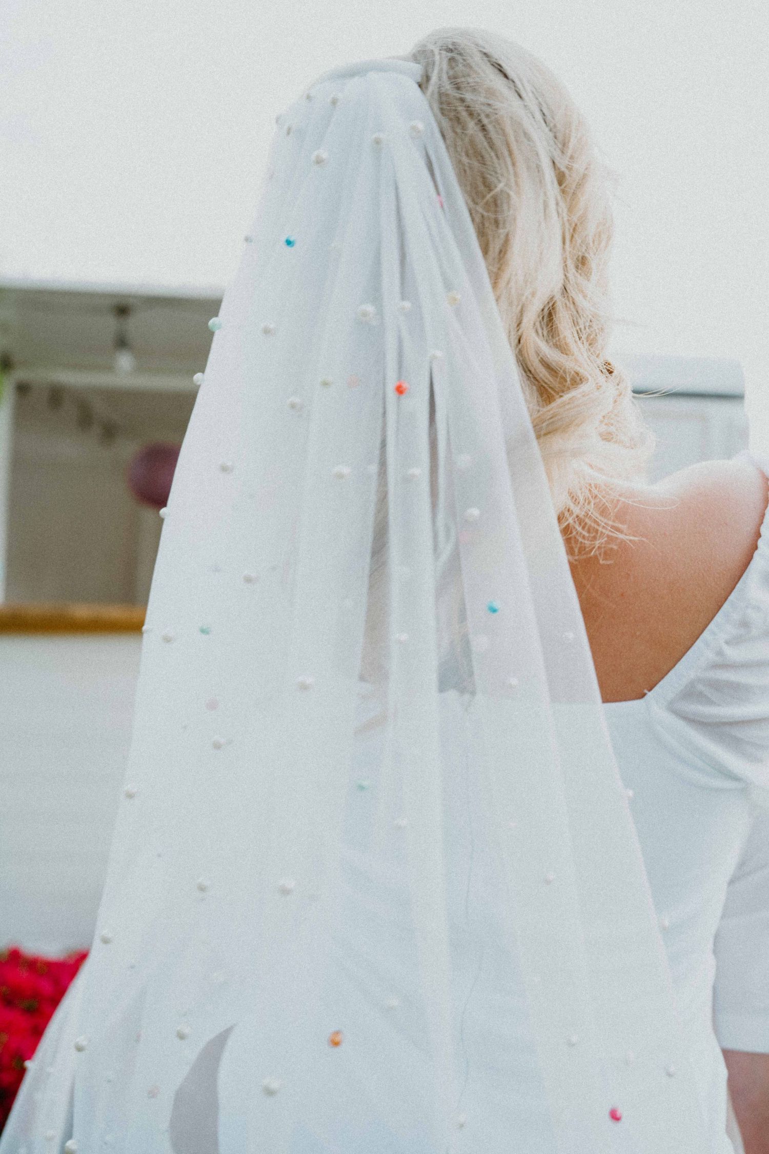 Close-up of bride's colorful pearl-dotted wedding veil with blonde hair and white off-shoulder dress.