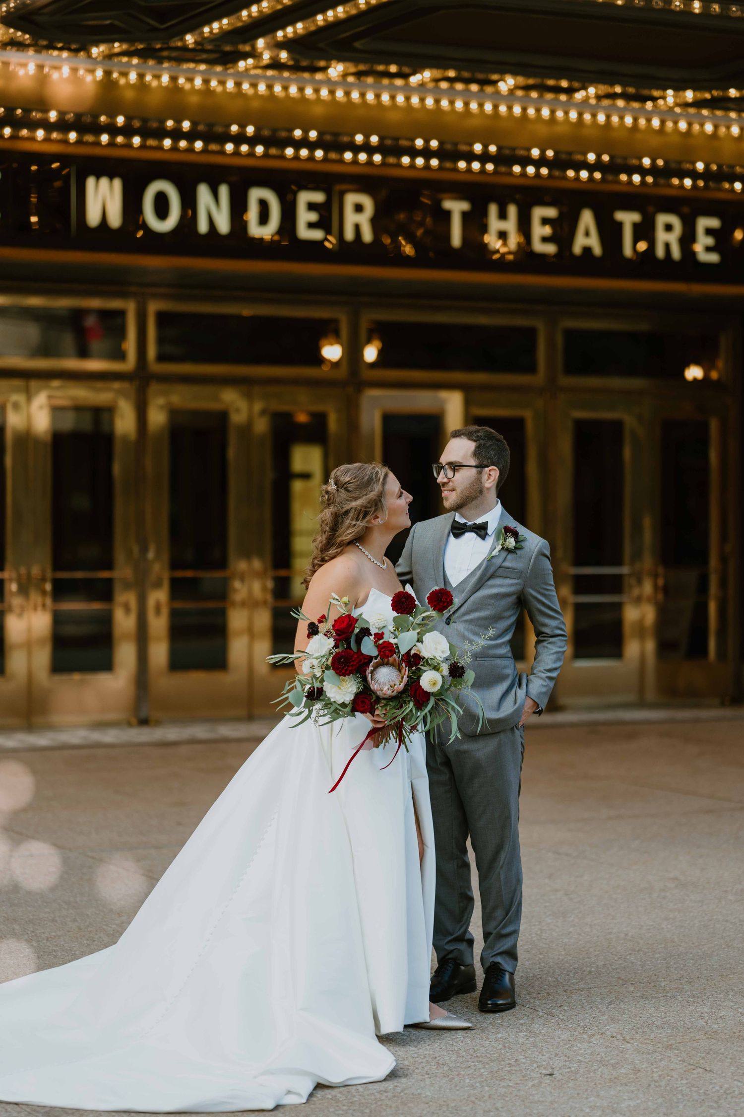 Bride and groom pose romantically in front of illuminated Wonder Theatre marquee at night.