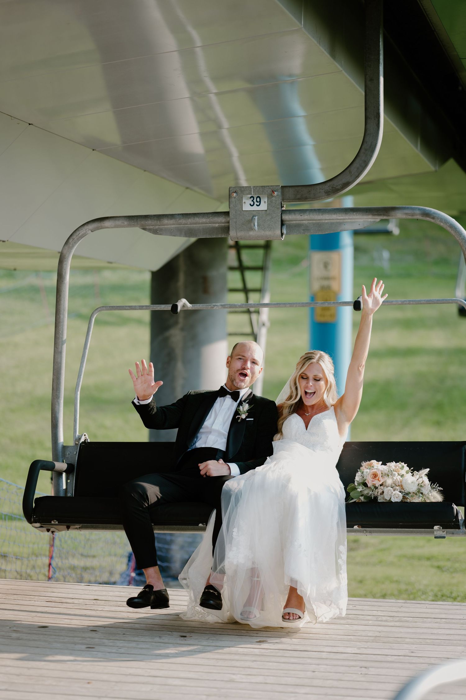 Excited bride and groom celebrating with raised hands while riding a ski lift at their wedding venue.