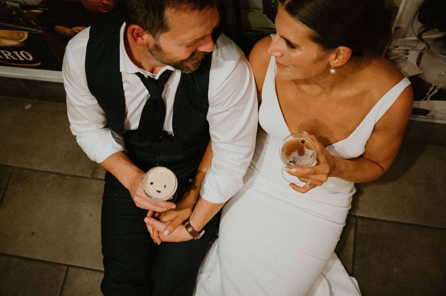 Overhead view of bride and groom sharing a sweet moment while holding espresso martini cocktails at wedding.