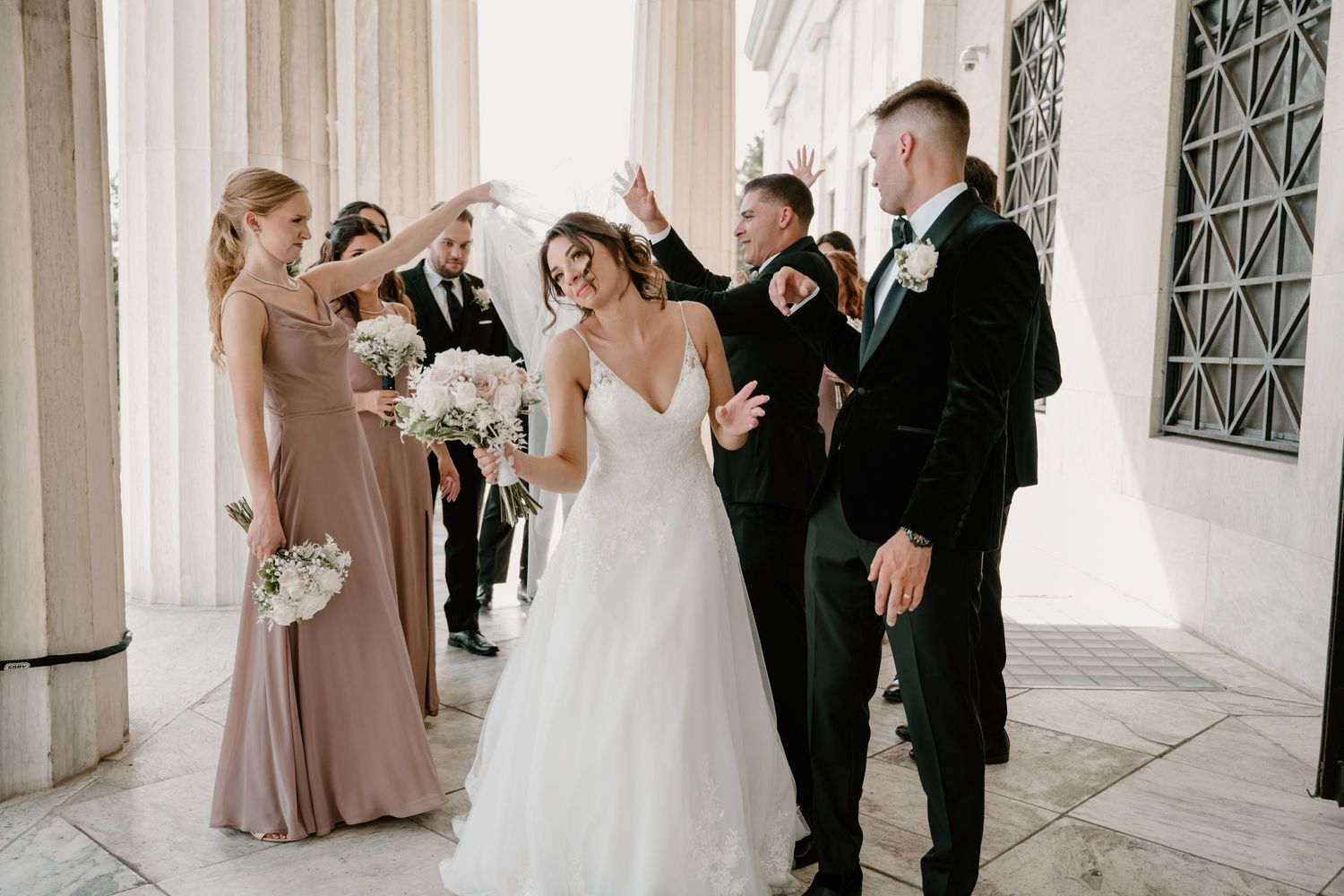 Joyful bride and groom celebrating with bridesmaids and groomsmen between grand columns.