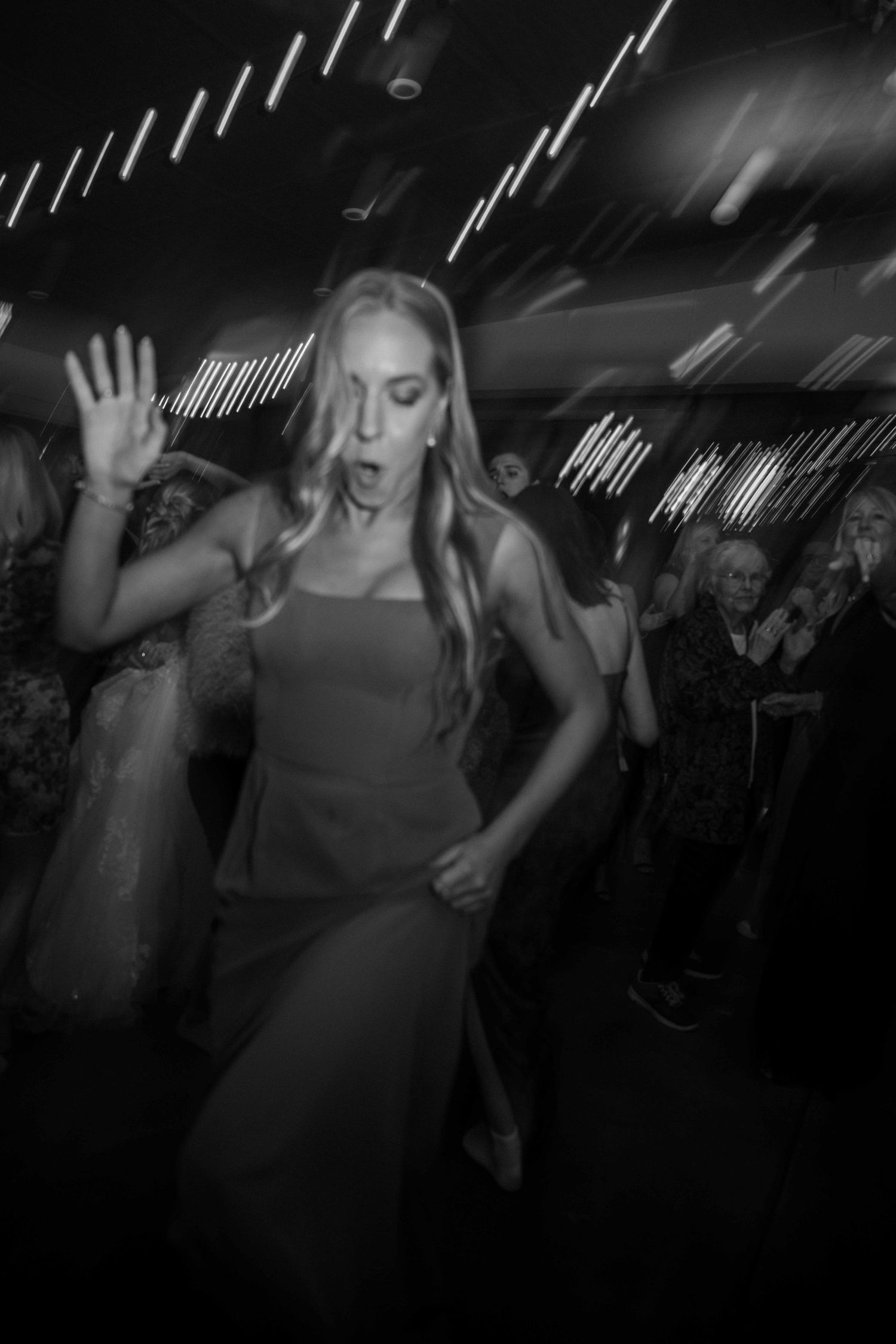 Black and white candid shot of a bridesmaid dancing energetically at a wedding reception.