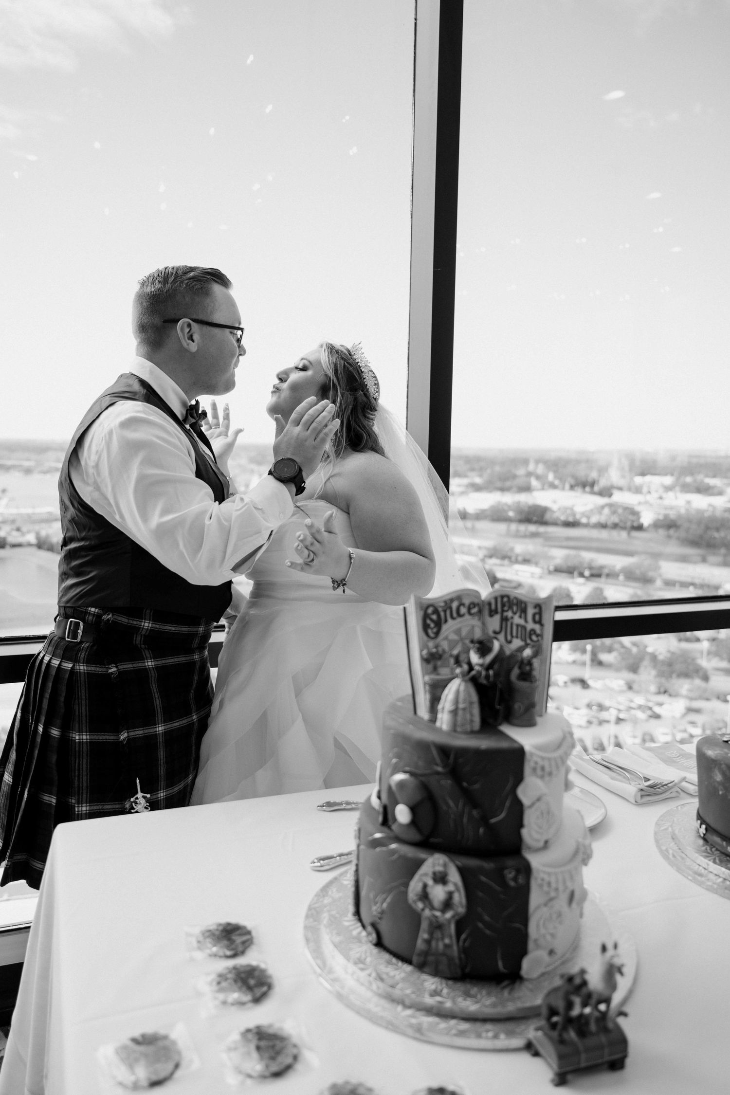 Bride and groom share tender moment beside tiered Disney-themed wedding cake in black and white.