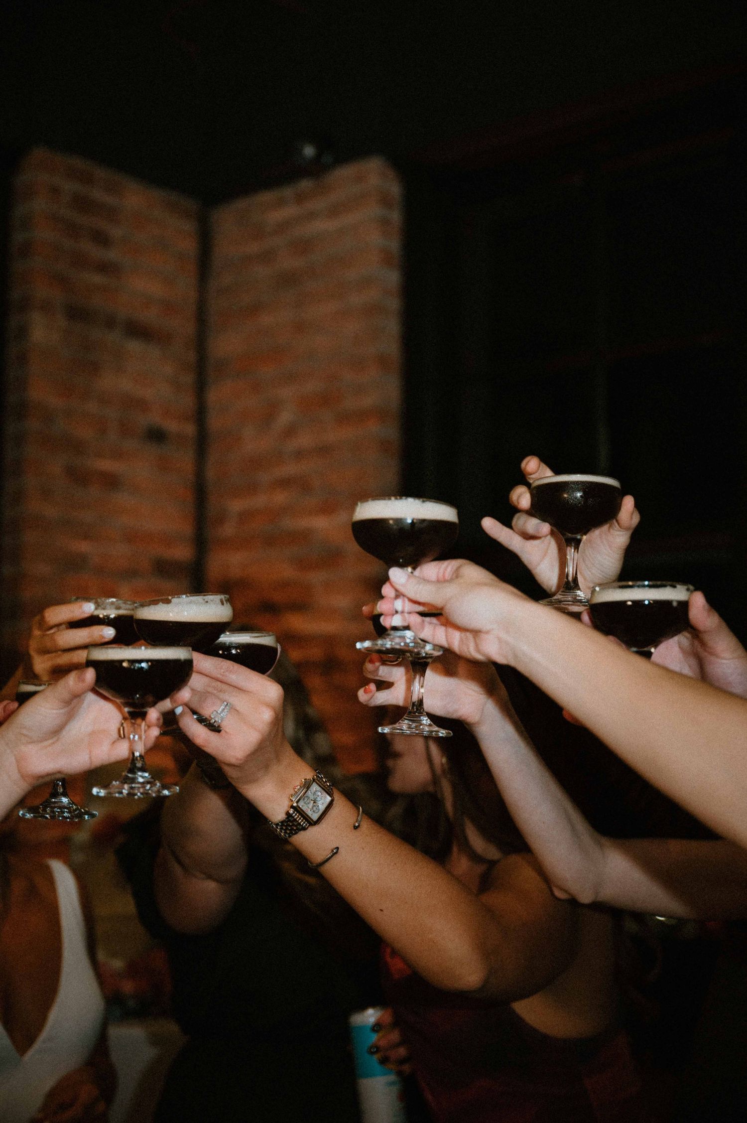 Wedding guests raise espresso martini cocktails in a celebratory toast at a reception party.