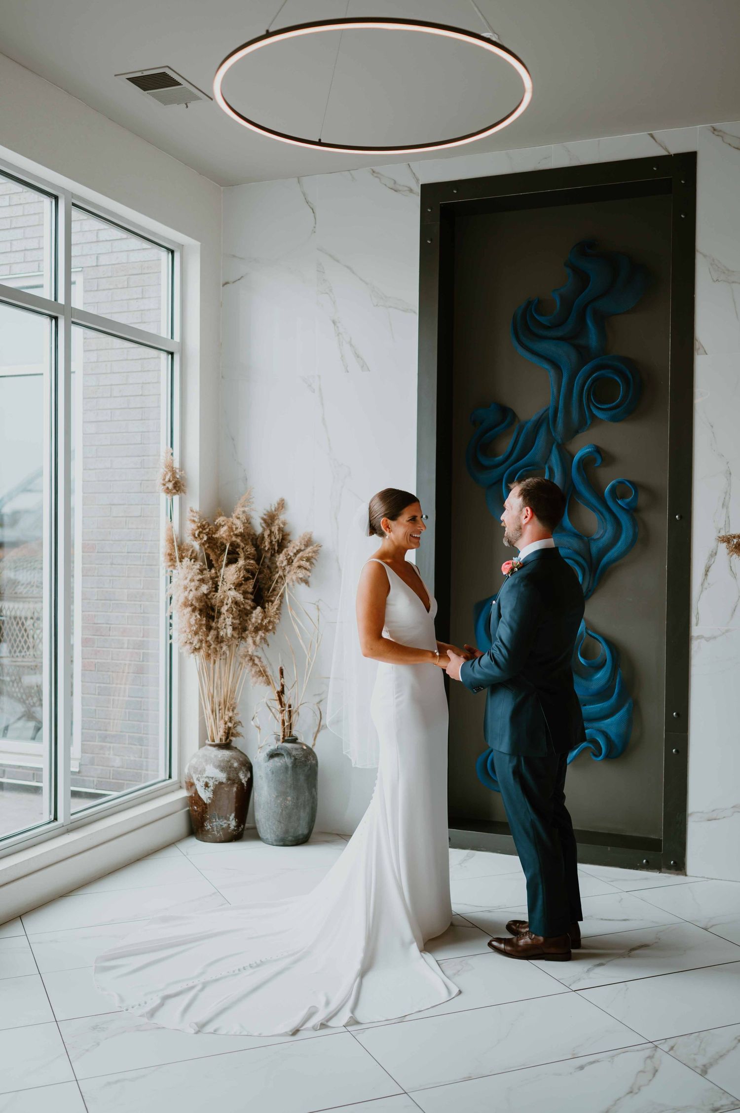 Bride and groom share first look in modern marble lobby with blue art.