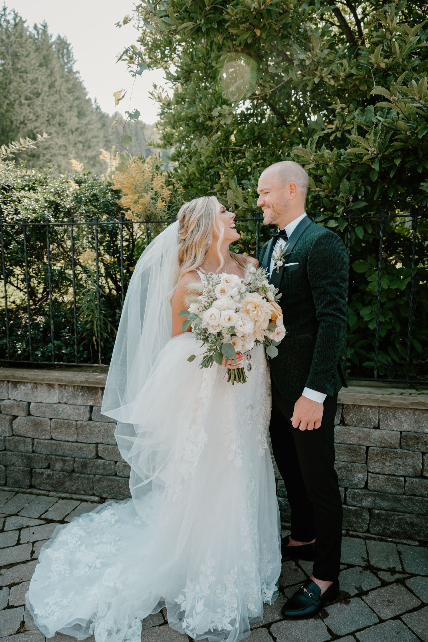 Bride and groom share romantic moment outdoors holding white floral bouquet.