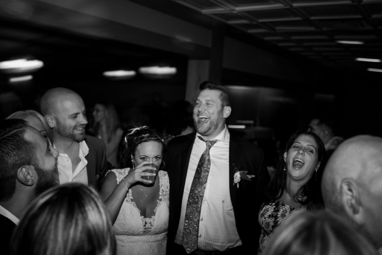 Black and white photo of bride and groom laughing joyfully with guests on the wedding dance floor.