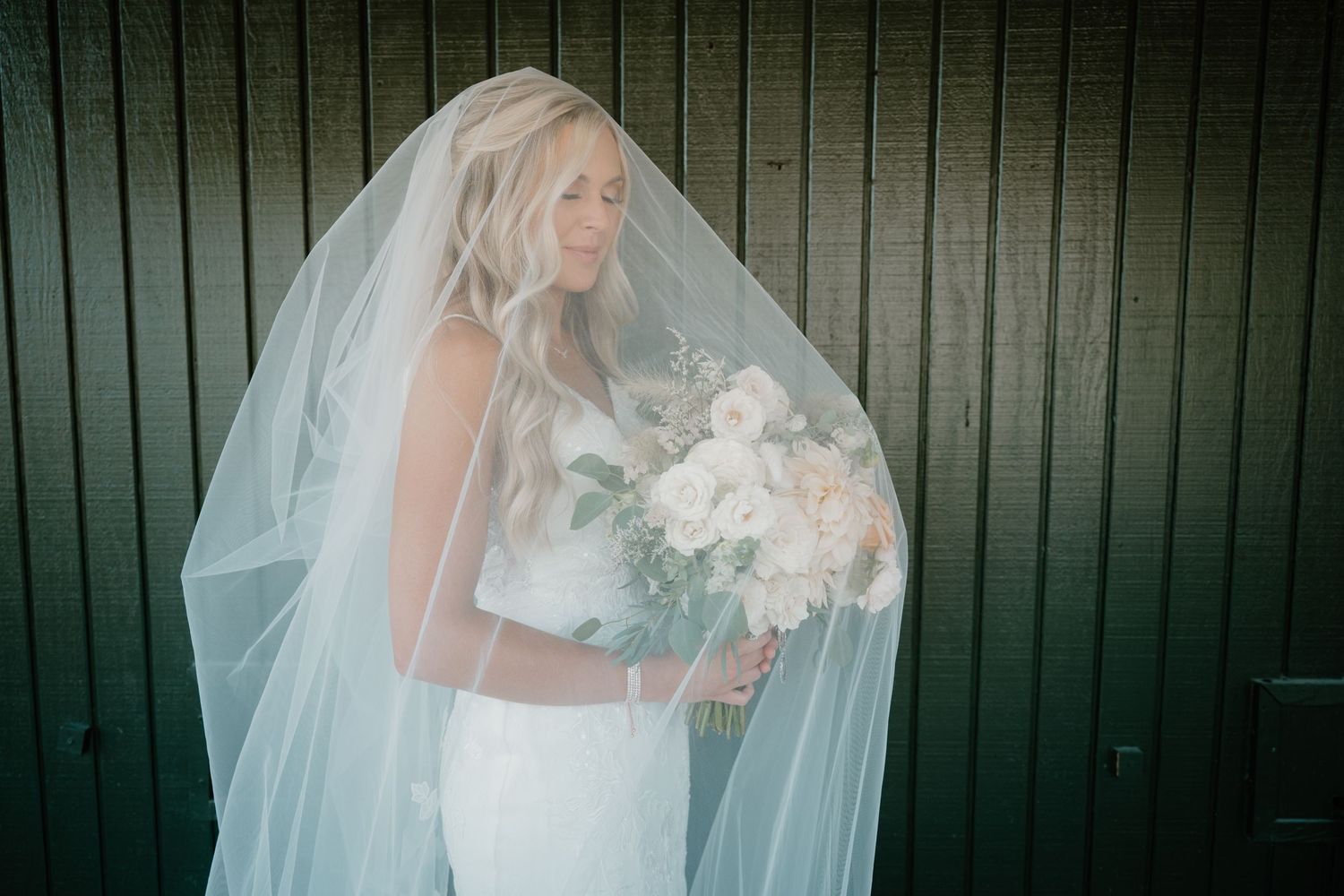 Bride in elegant white gown holding bouquet of white flowers under flowing veil.