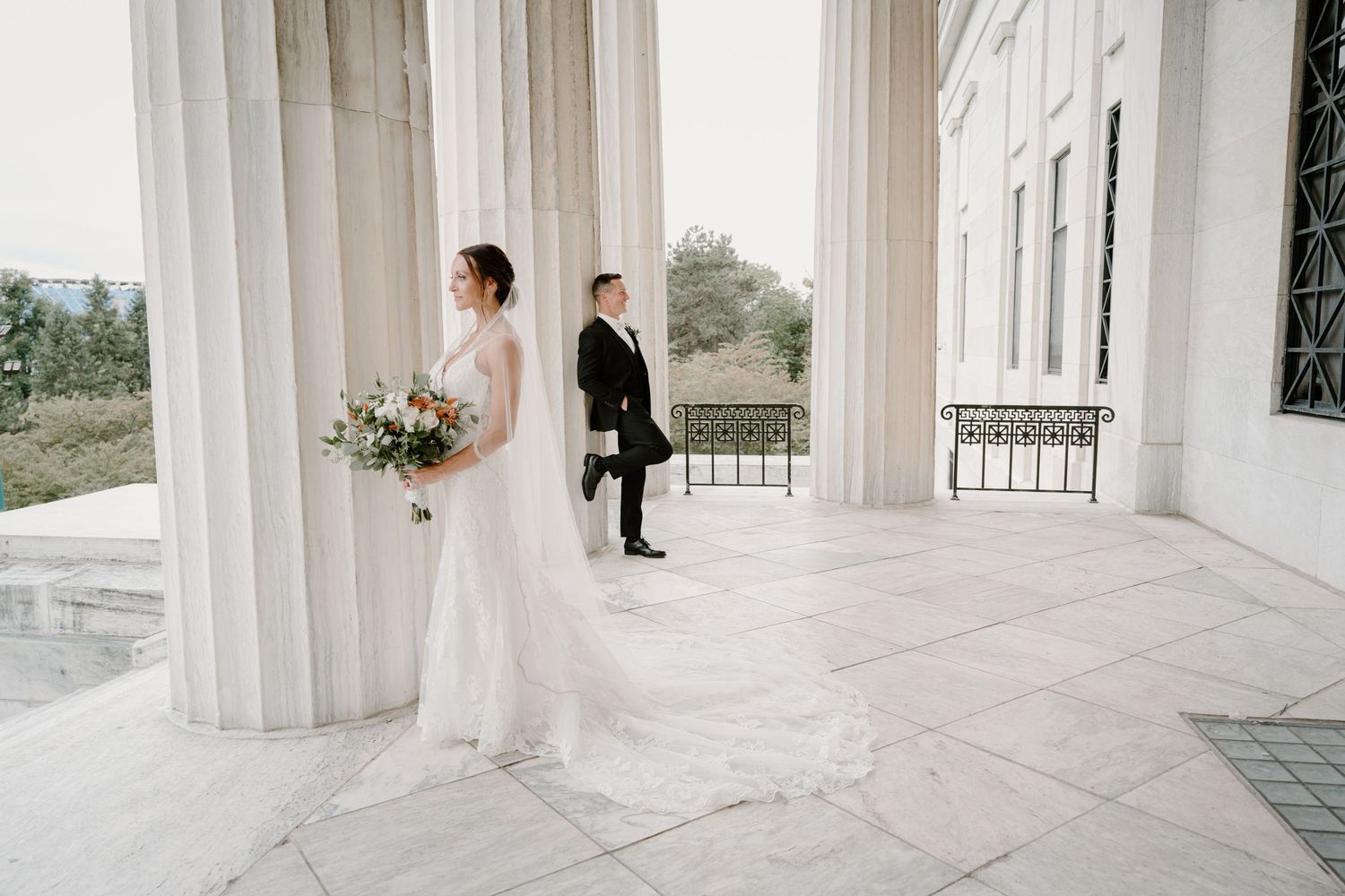 Bride and groom share a romantic first look moment between elegant white columns at a classic wedding venue.