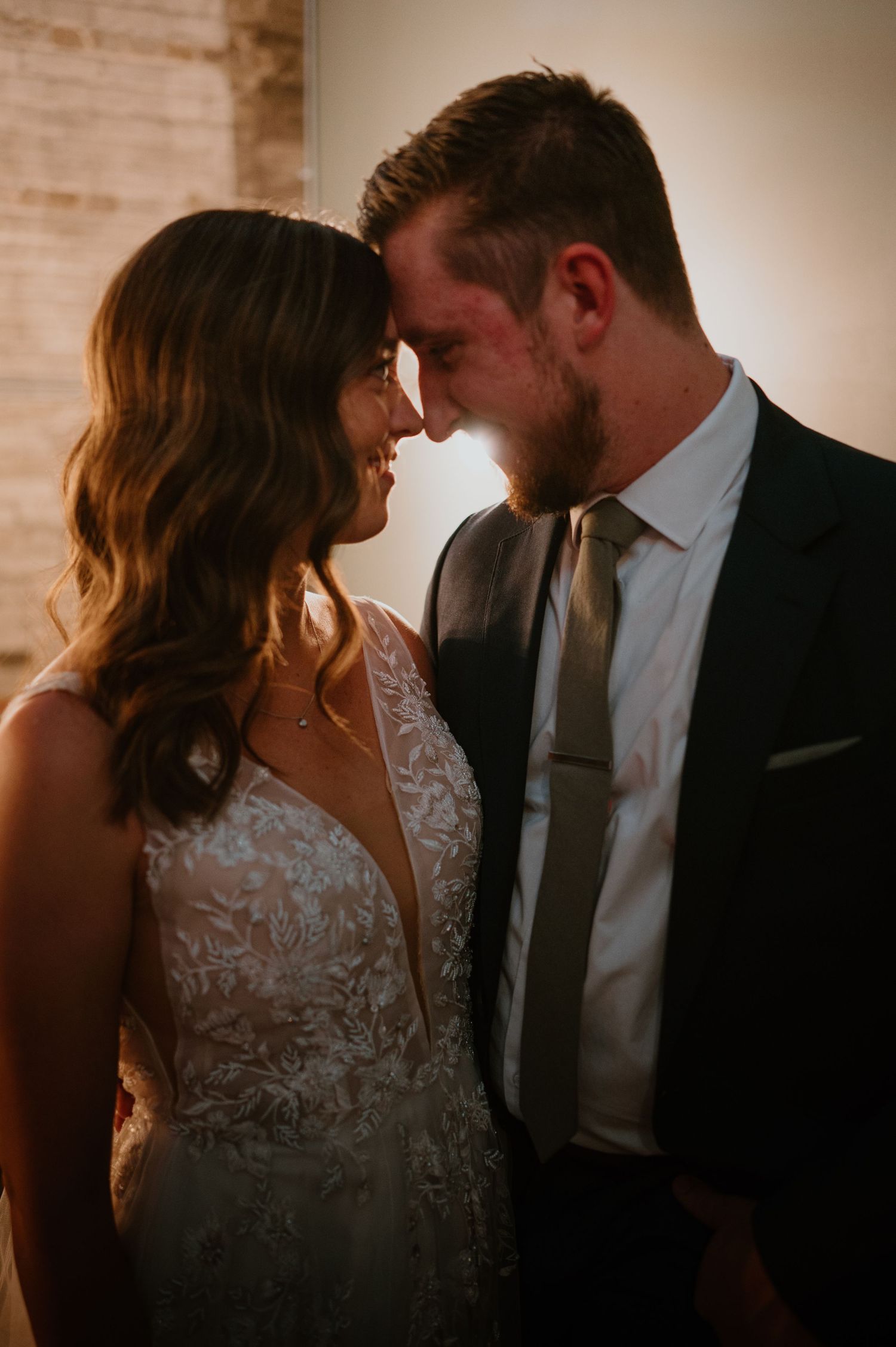 Bride and groom sharing intimate forehead touch moment in warm golden light.