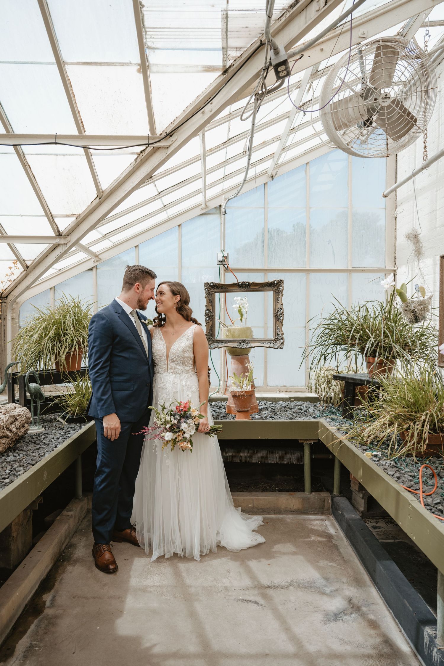Bride and groom sharing romantic moment inside lush greenhouse wedding venue.