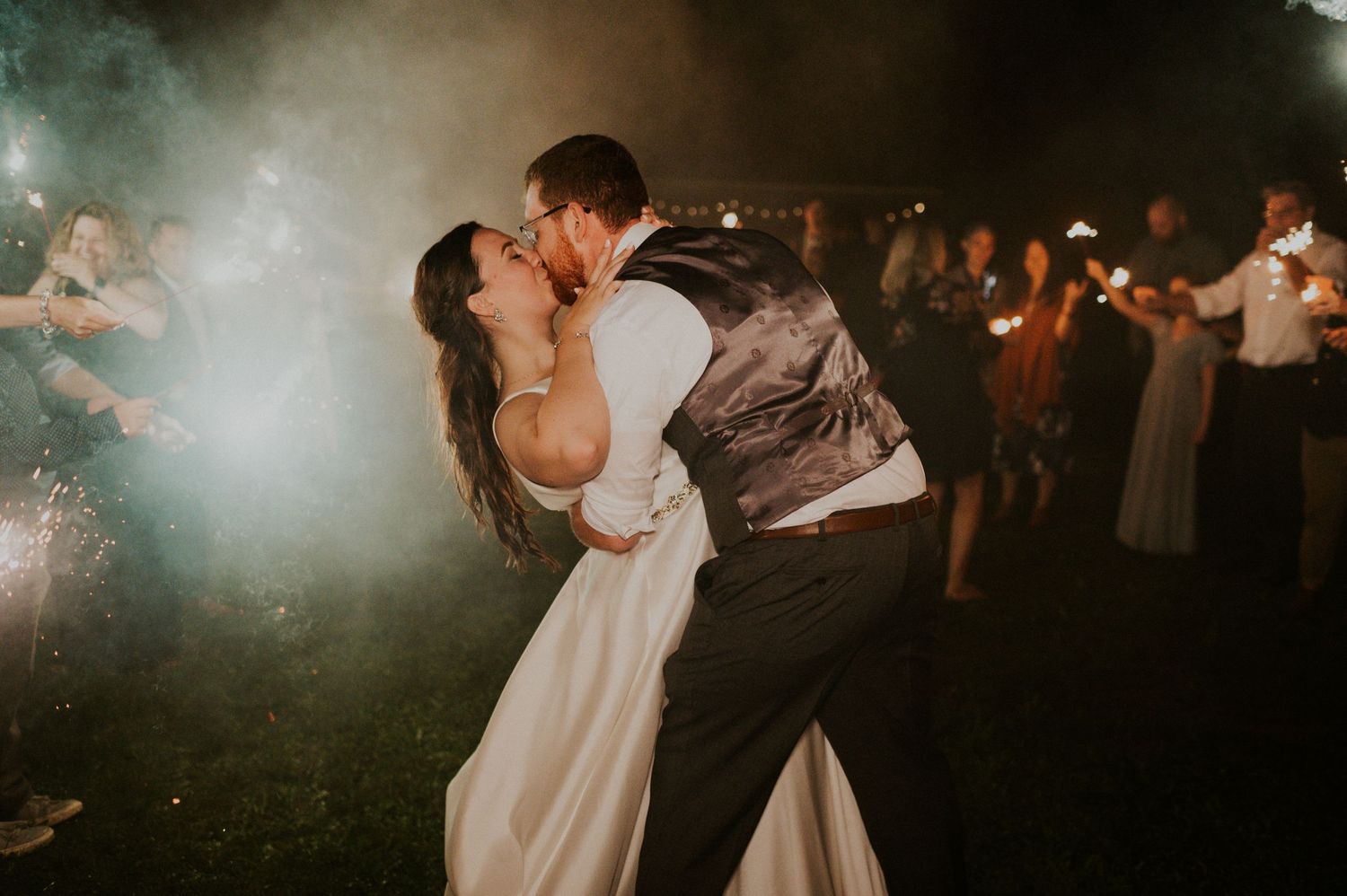 Bride and groom sharing a passionate kiss on the dance floor surrounded by sparklers at night.