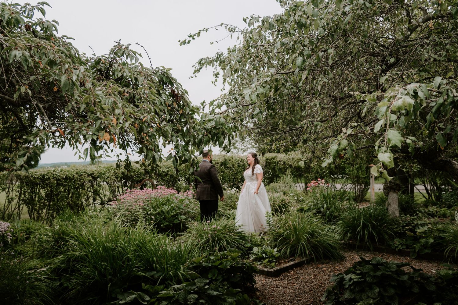 Bride and groom holding hands in a lush garden surrounded by greenery on their wedding day.