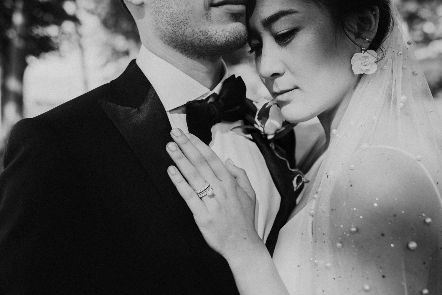 Romantic black and white close-up of bride and groom embracing, bride wearing pearl veil and ring.