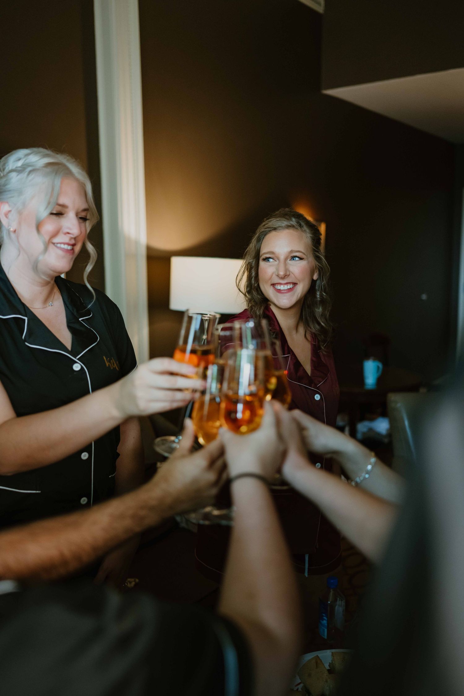 Bride and bridesmaids in black pajamas toast with champagne glasses during wedding morning preparations.