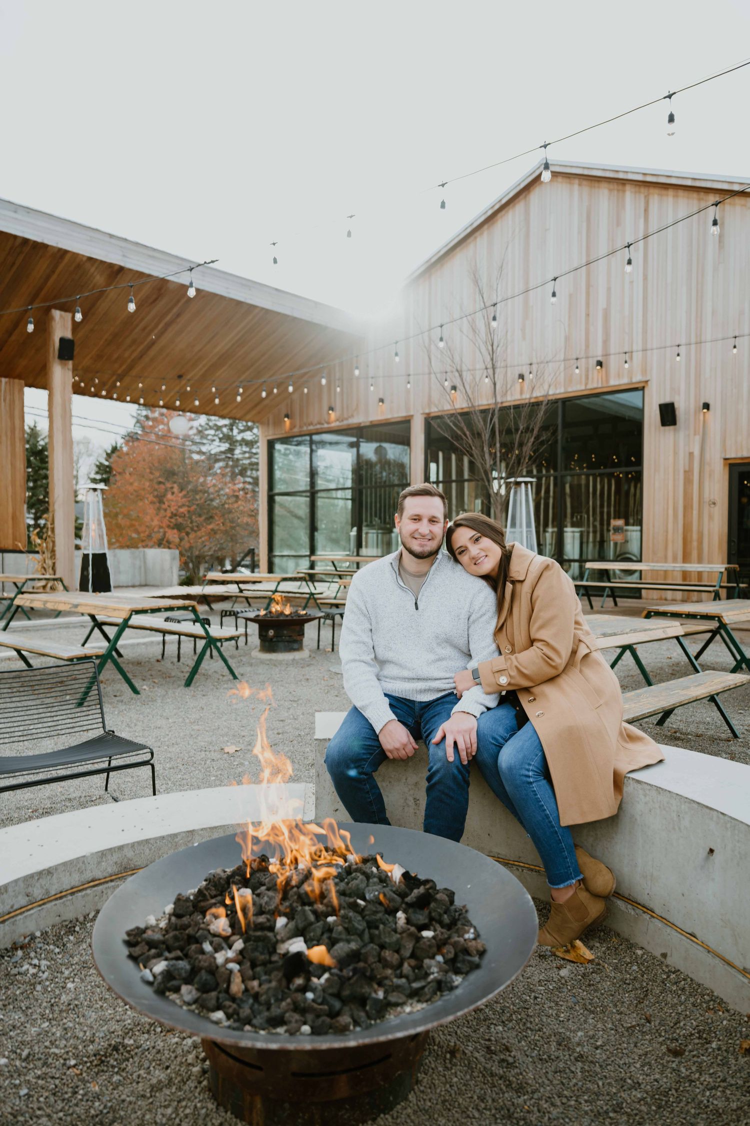 Smiling couple sits together by outdoor fire pit at modern wood-clad venue.