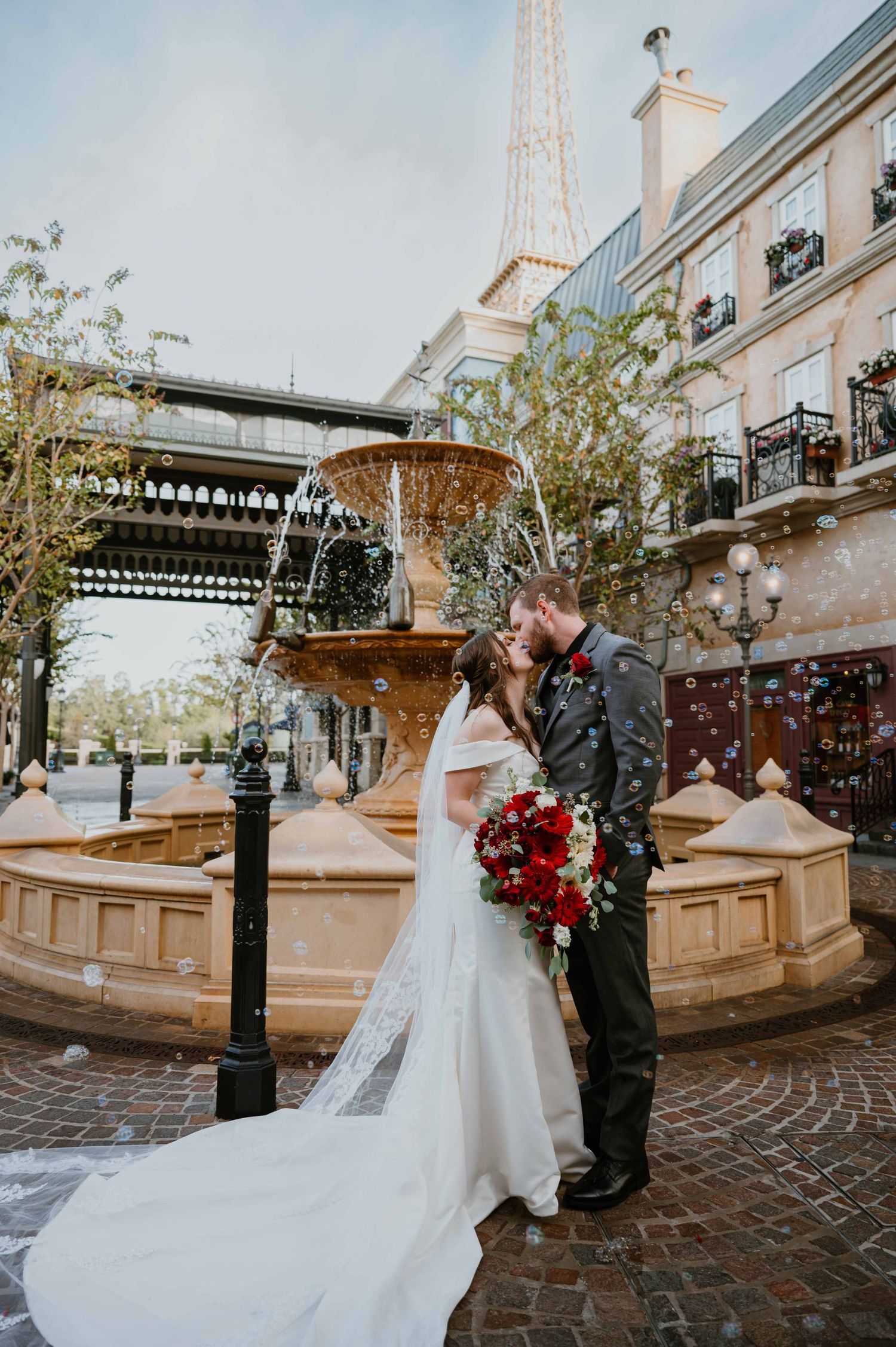 Couple shares a romantic kiss near a stone fountain with the Eiffel Tower visible at Epcot France pavilion.