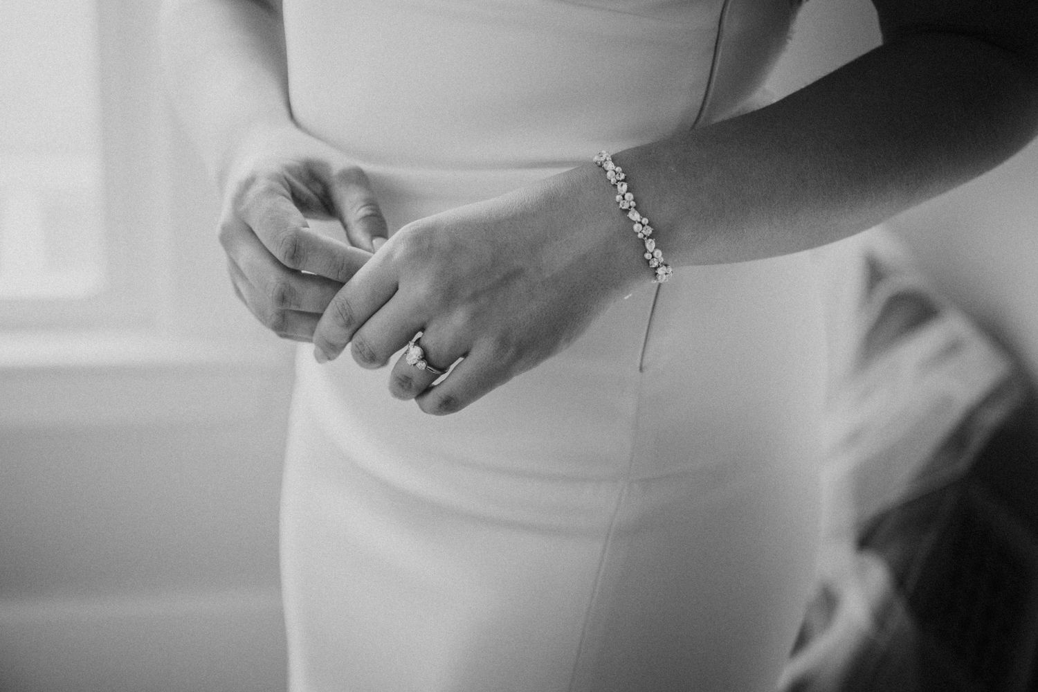 Black and white close-up of bride in fitted wedding dress wearing pearl bracelet and diamond ring.