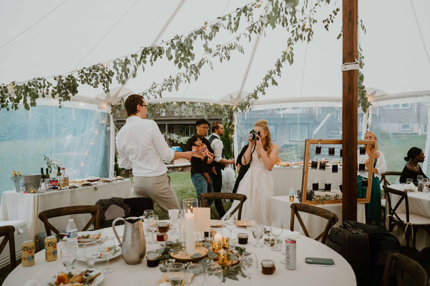Bride and groom mingle with guests under a clear tent at elegant outdoor wedding reception.