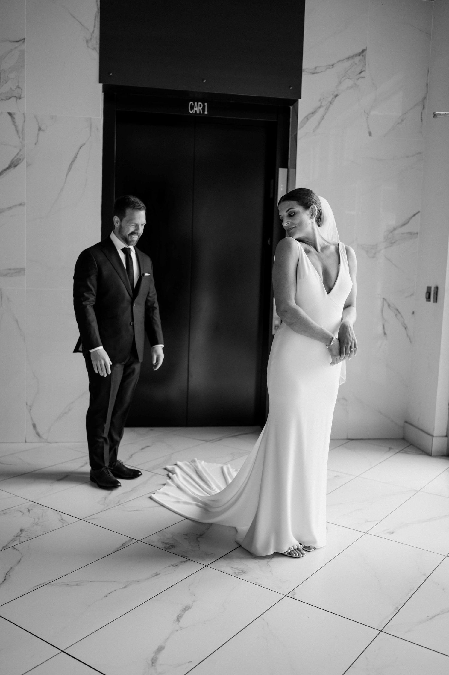 Black and white photo of bride and groom near marble elevator doors.