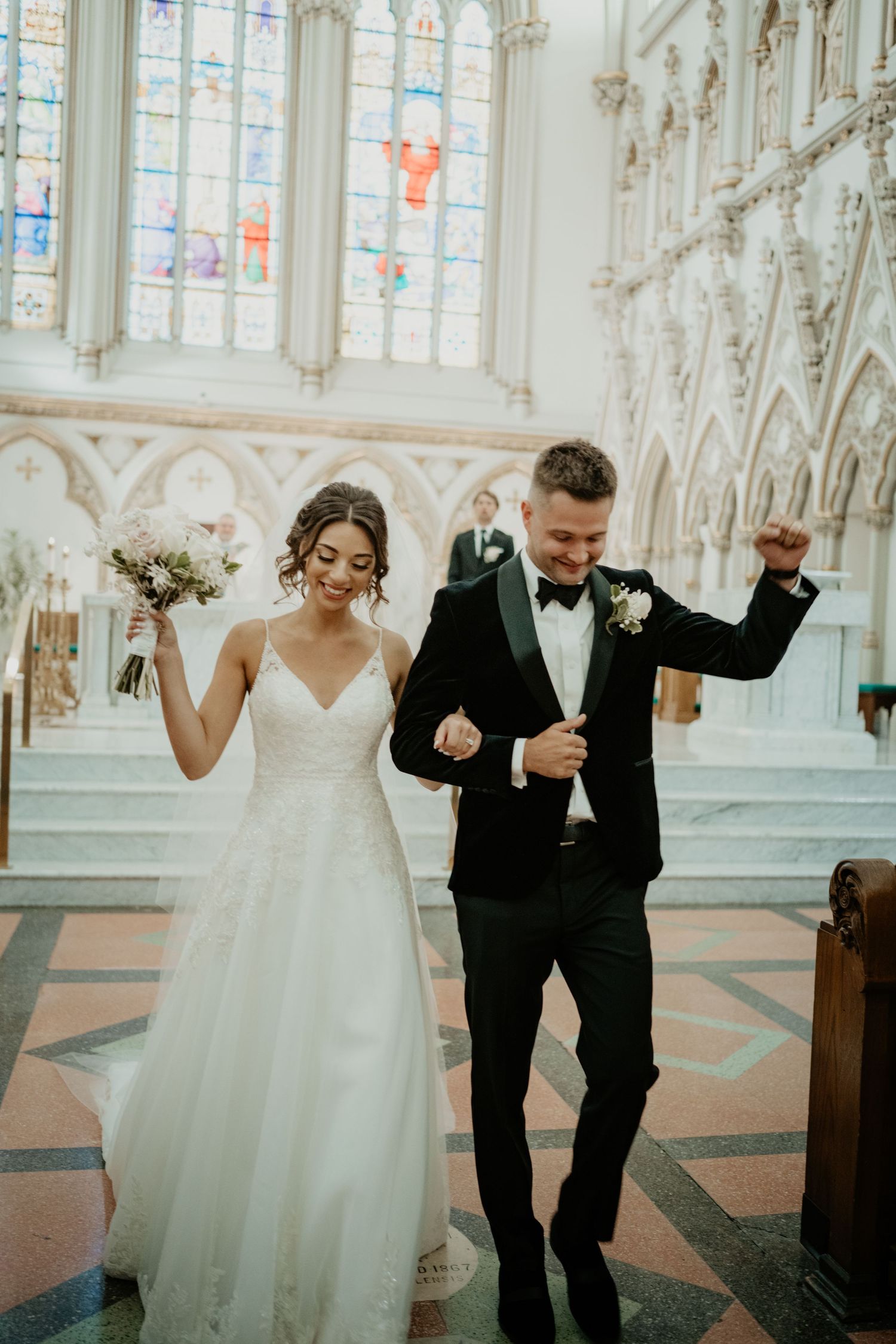 Jubilant newlyweds celebrating as they walk down the aisle of a beautiful Gothic church after ceremony.
