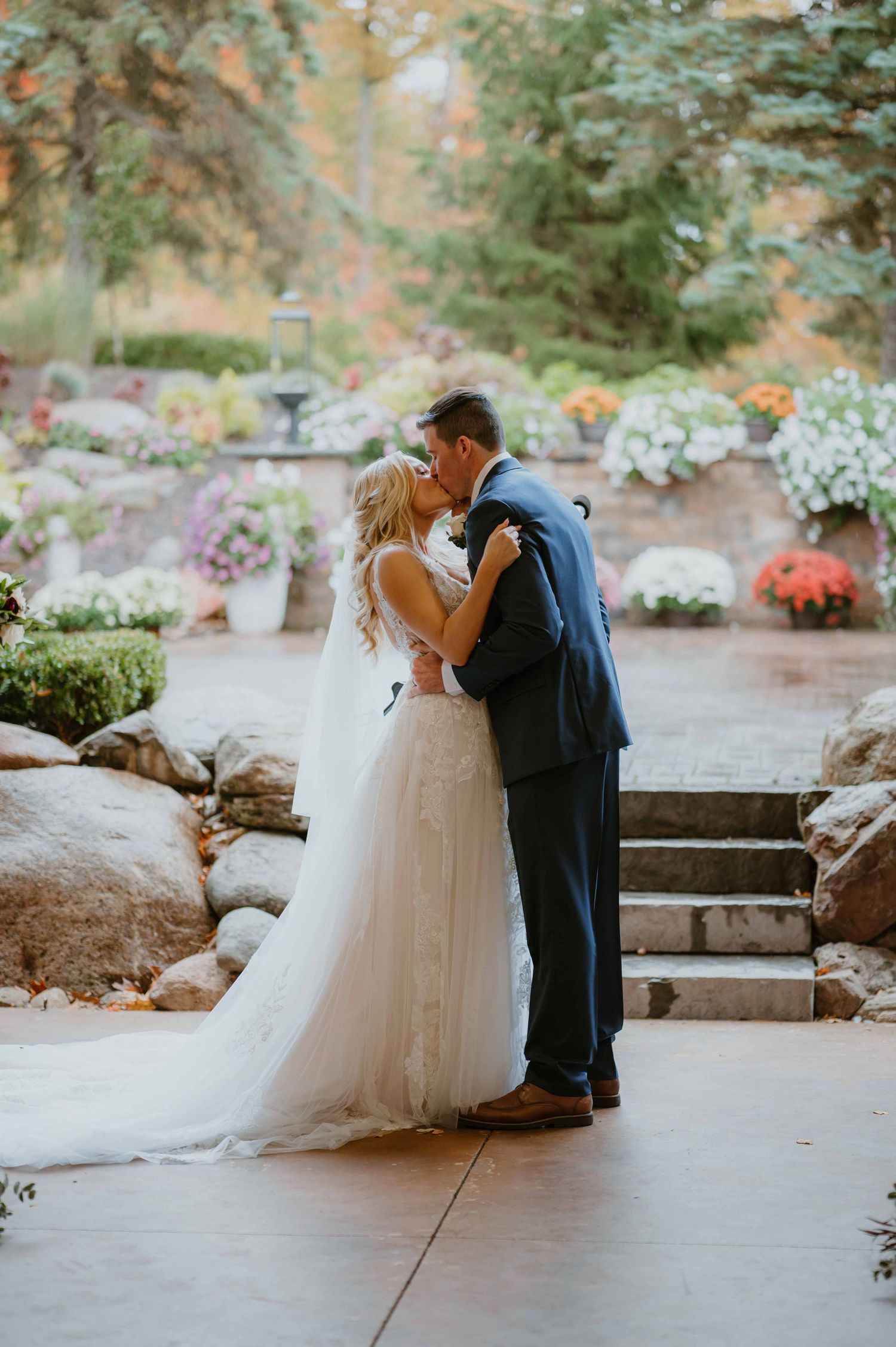 Bride and groom sharing first kiss surrounded by colorful autumn flowers at garden wedding.