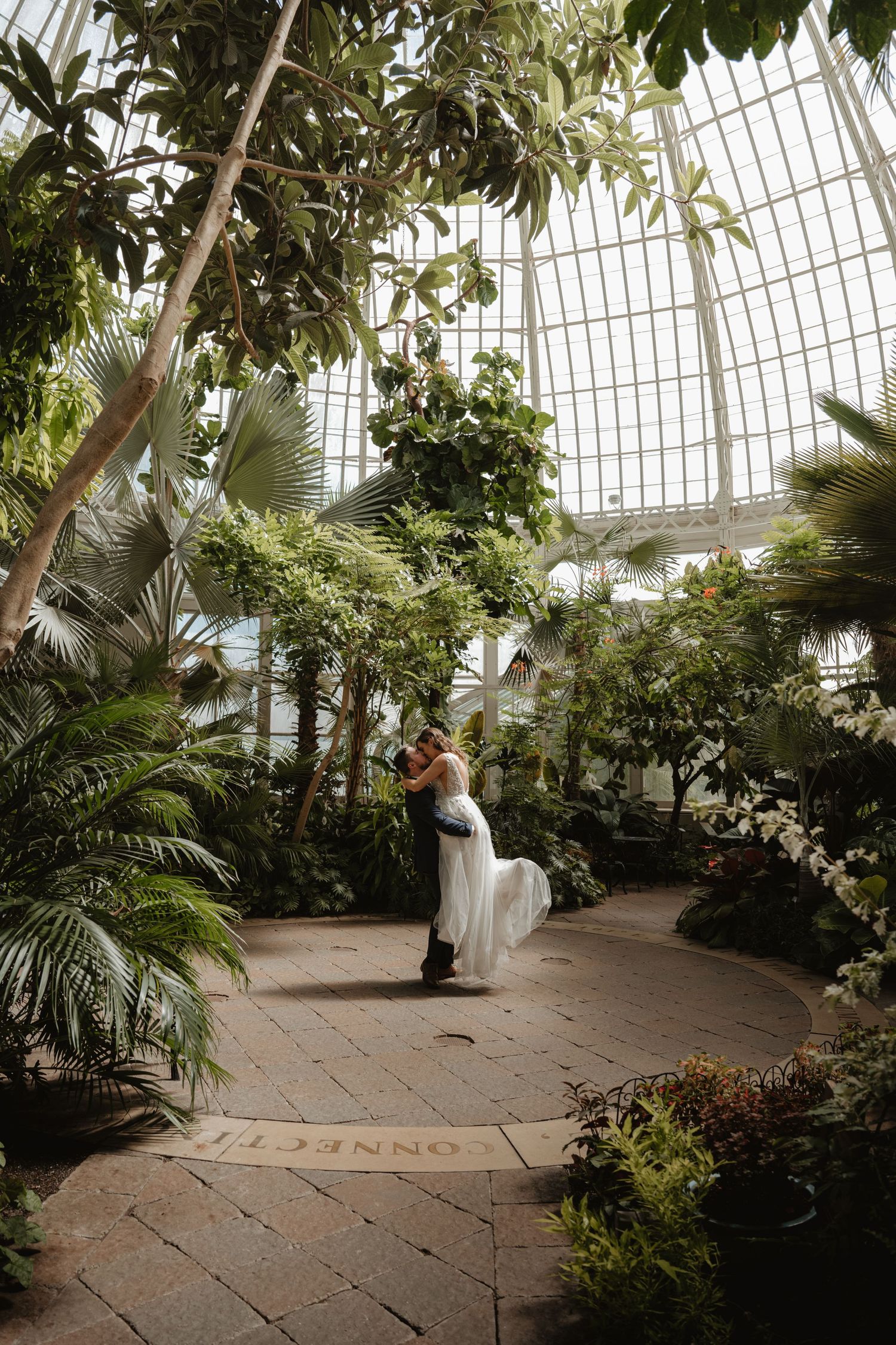 Bride and groom dancing and spinning in a stunning tropical greenhouse conservatory.
