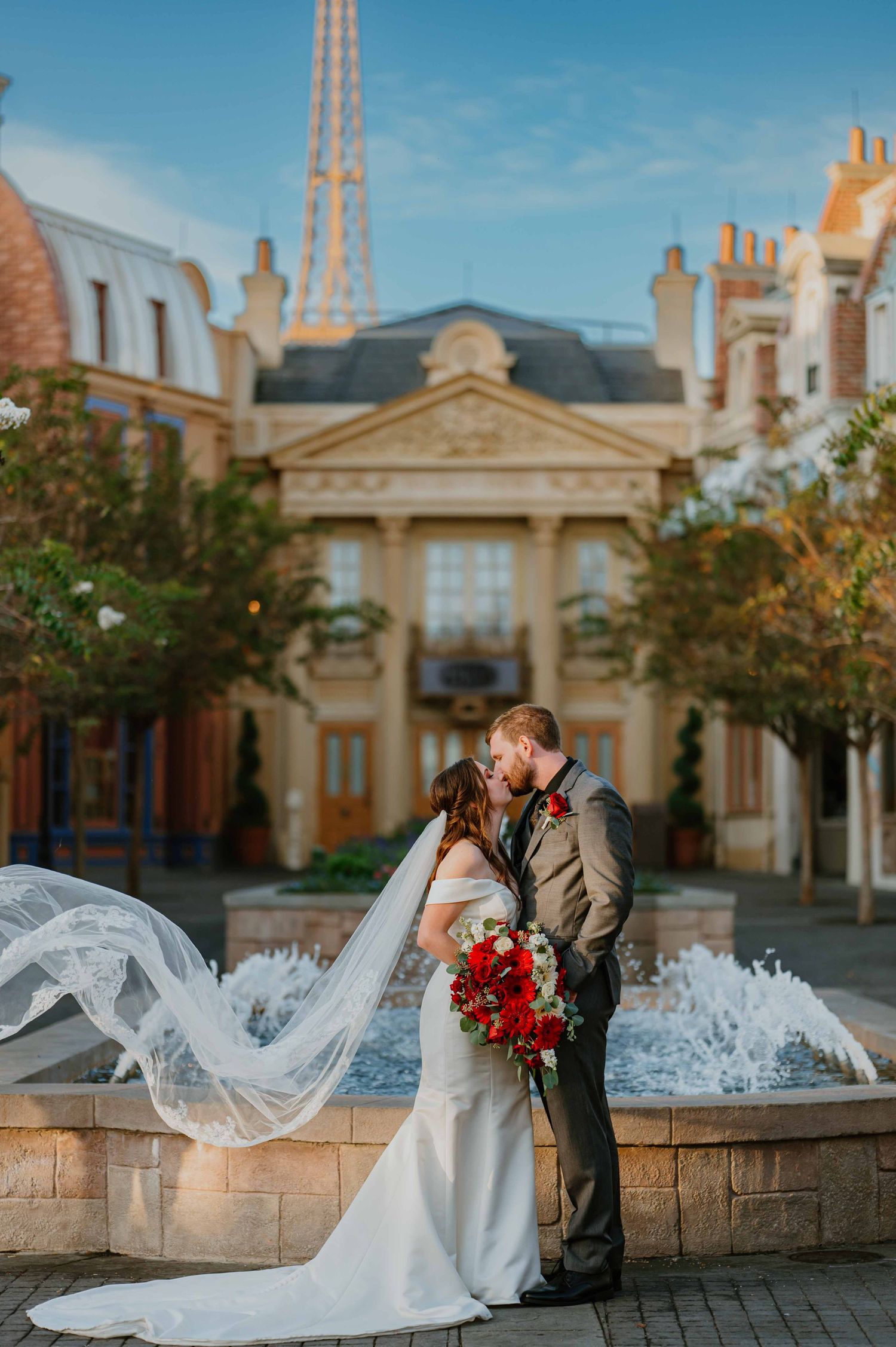 Bride and groom share a kiss as her veil flows dramatically by the France pavilion fountain at Epcot.