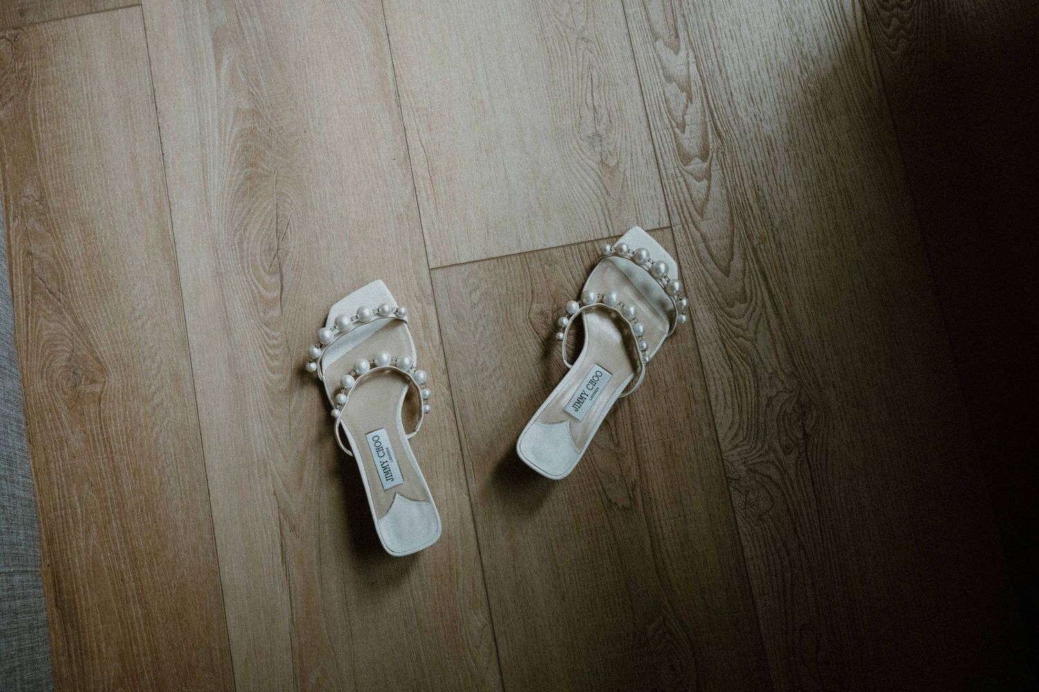 White pearl-embellished bridal sandals on a wooden floor.