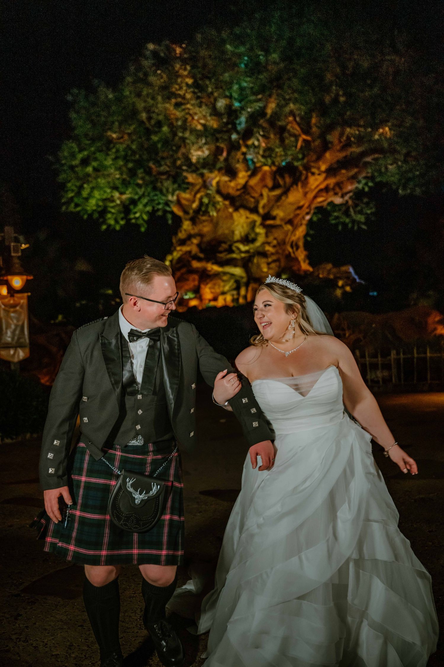 Newlywed couple laughing together in front of the glowing Tree of Life at Walt Disney World's Animal Kingdom.