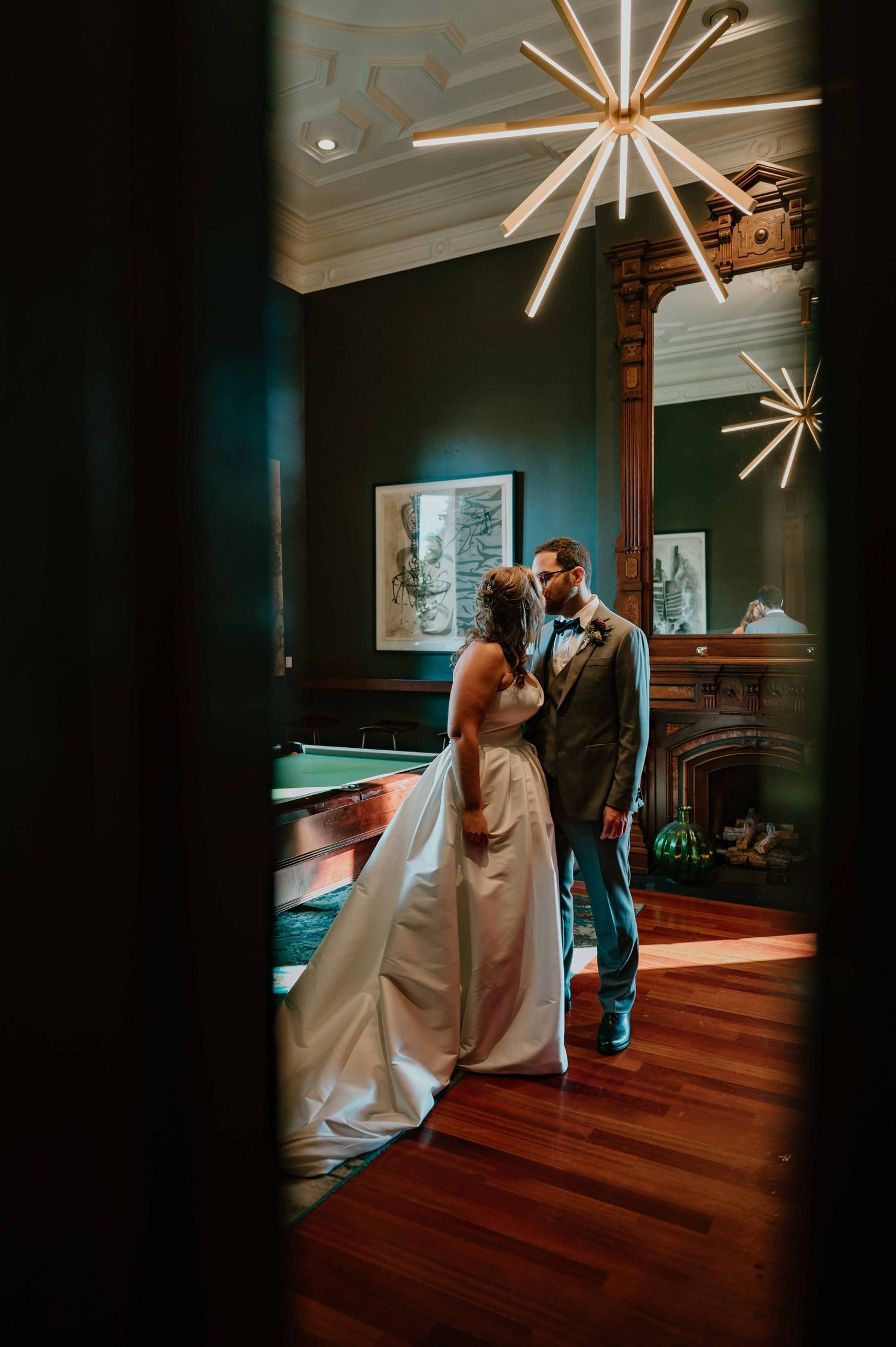 Bride and groom share an intimate moment in an elegant dark green room with a starburst chandelier.
