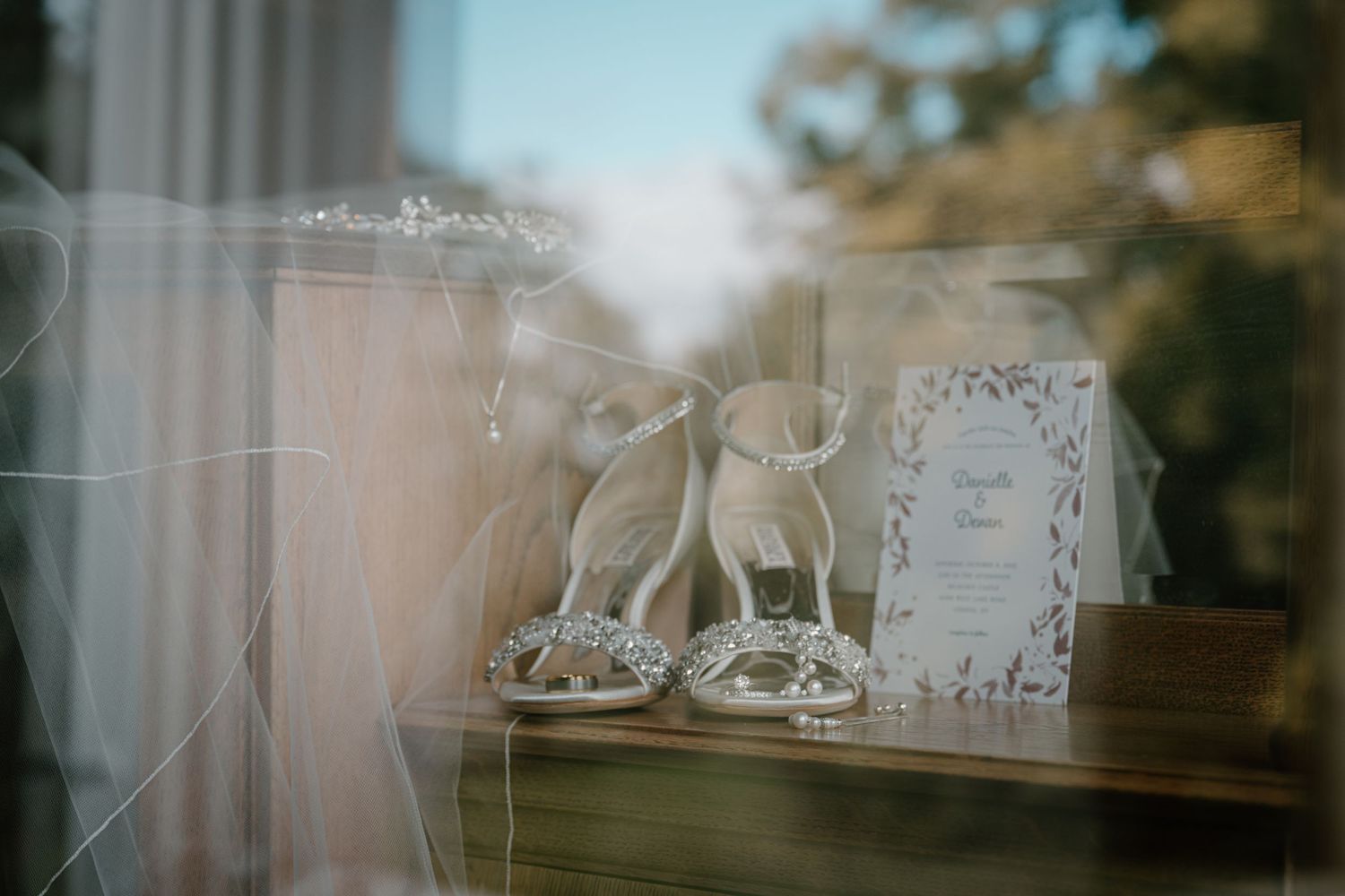 Elegant bridal details including sparkling heels, a tiara, and wedding invitation displayed on a wooden table.