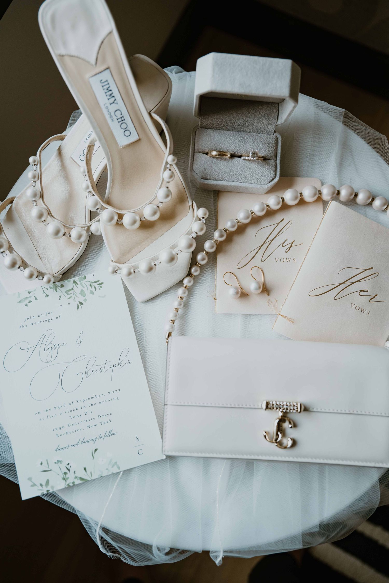 Jimmy Choo pearl heels, rings, vows booklets, and pearl necklace styled on wedding flat lay.